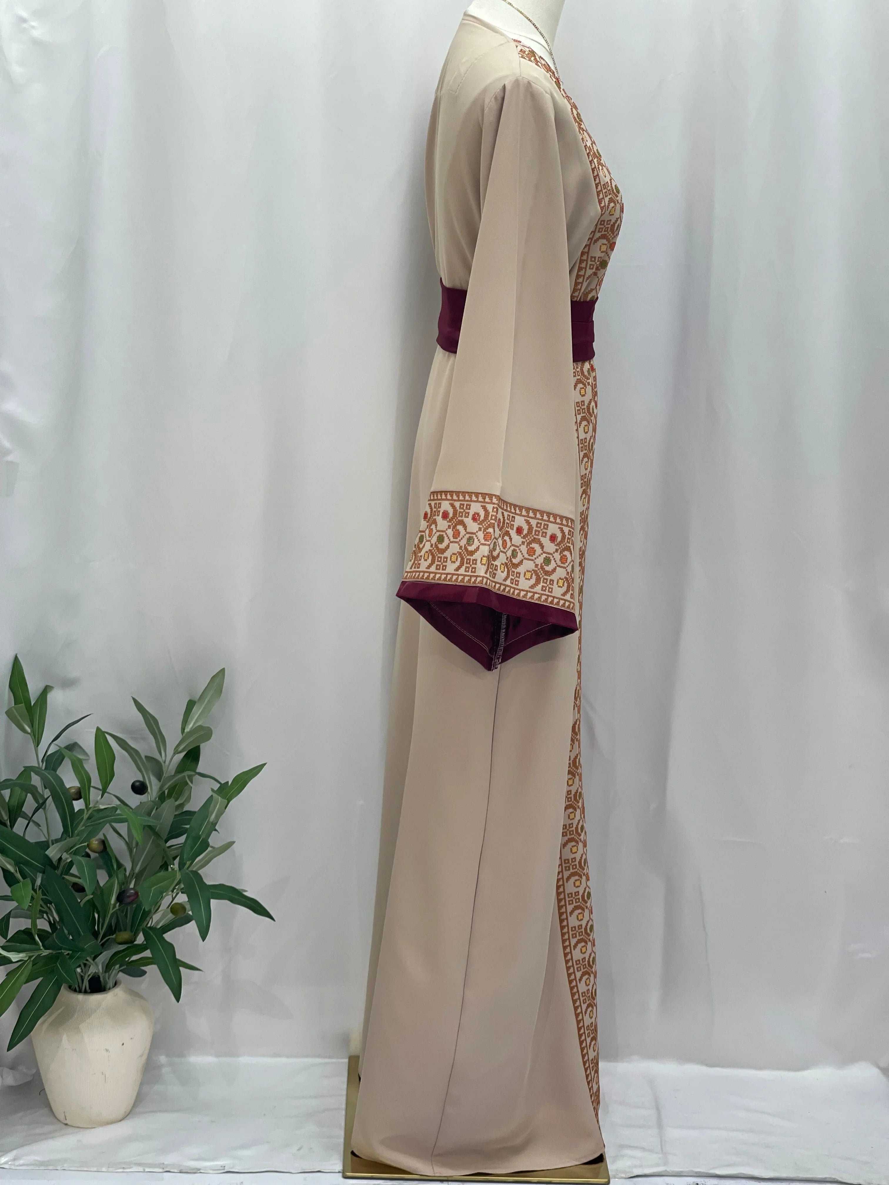 Palestinian Elegance Embroiderd Thobe With Belt in beige with intricate embroidery and maroon belt on mannequin