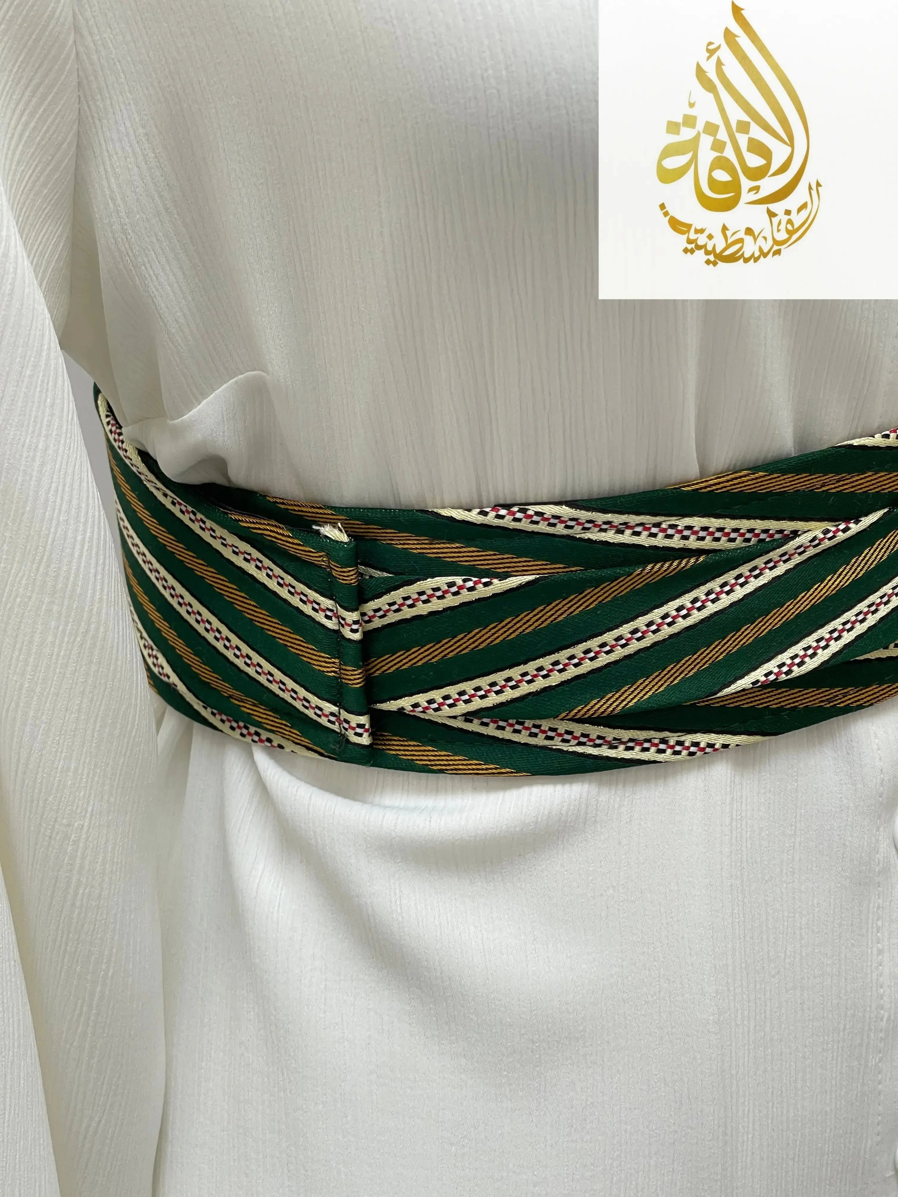 Green and gold Palestinian embroidered belt wrapped around white fabric from Palestinian Elegance accessories