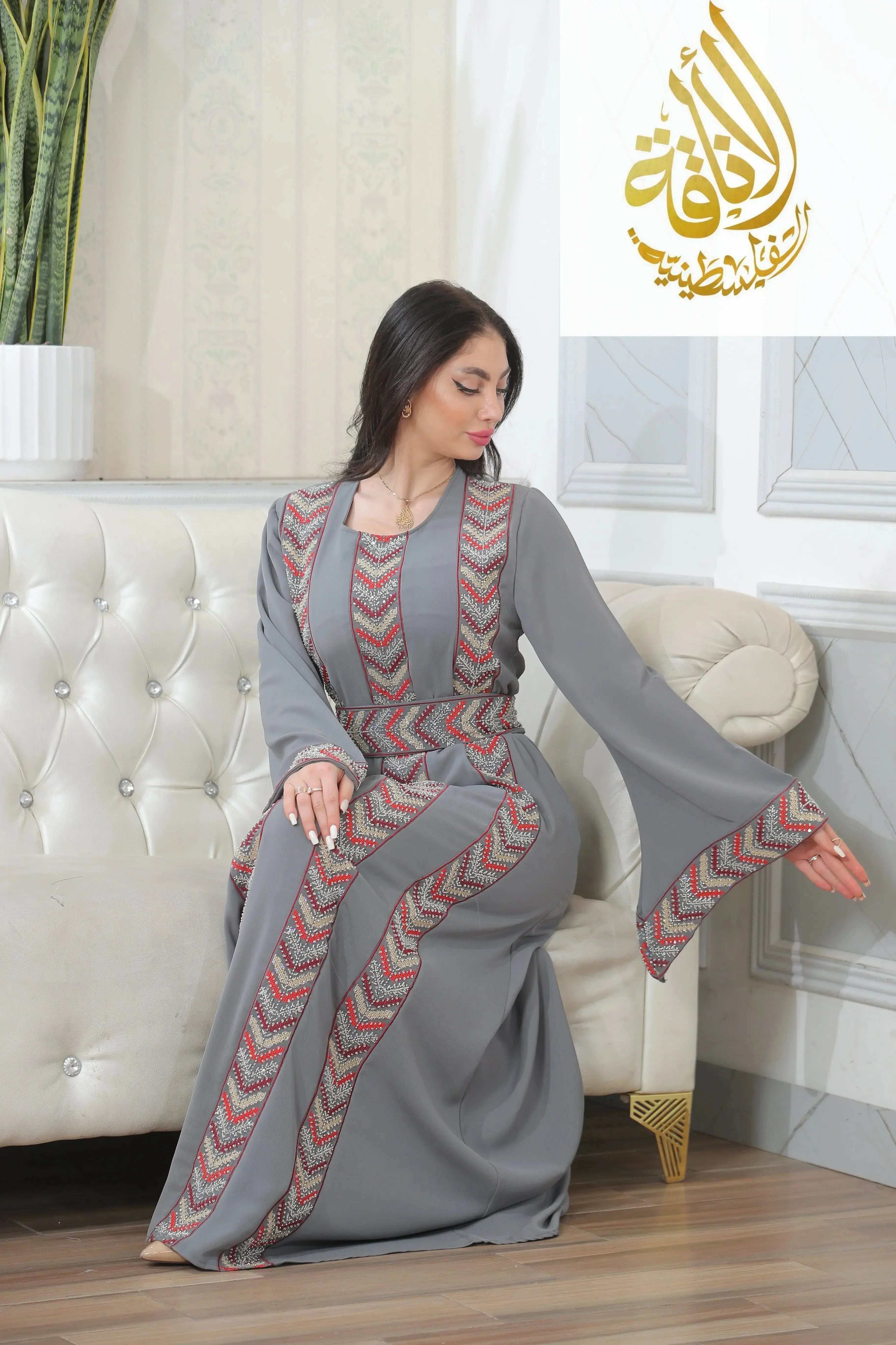 Palestinian Elegance Seham Embroidered Beads Thoub in gray with detailed red and white embroidery worn by a seated woman