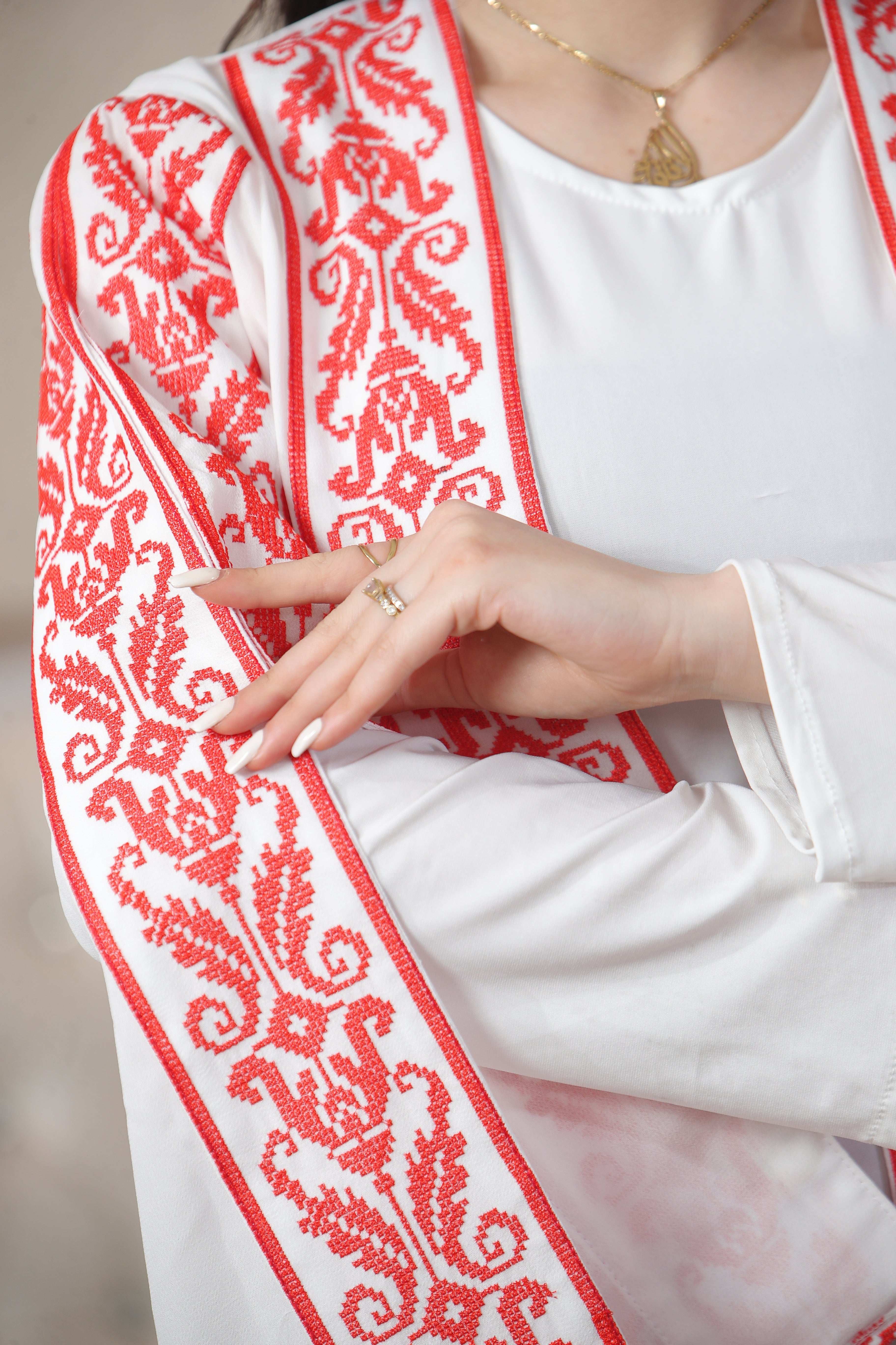 Close-up of Shereen Embroidered Bisht Abaya with red intricate embroidery on white fabric by Palestinian Elegance