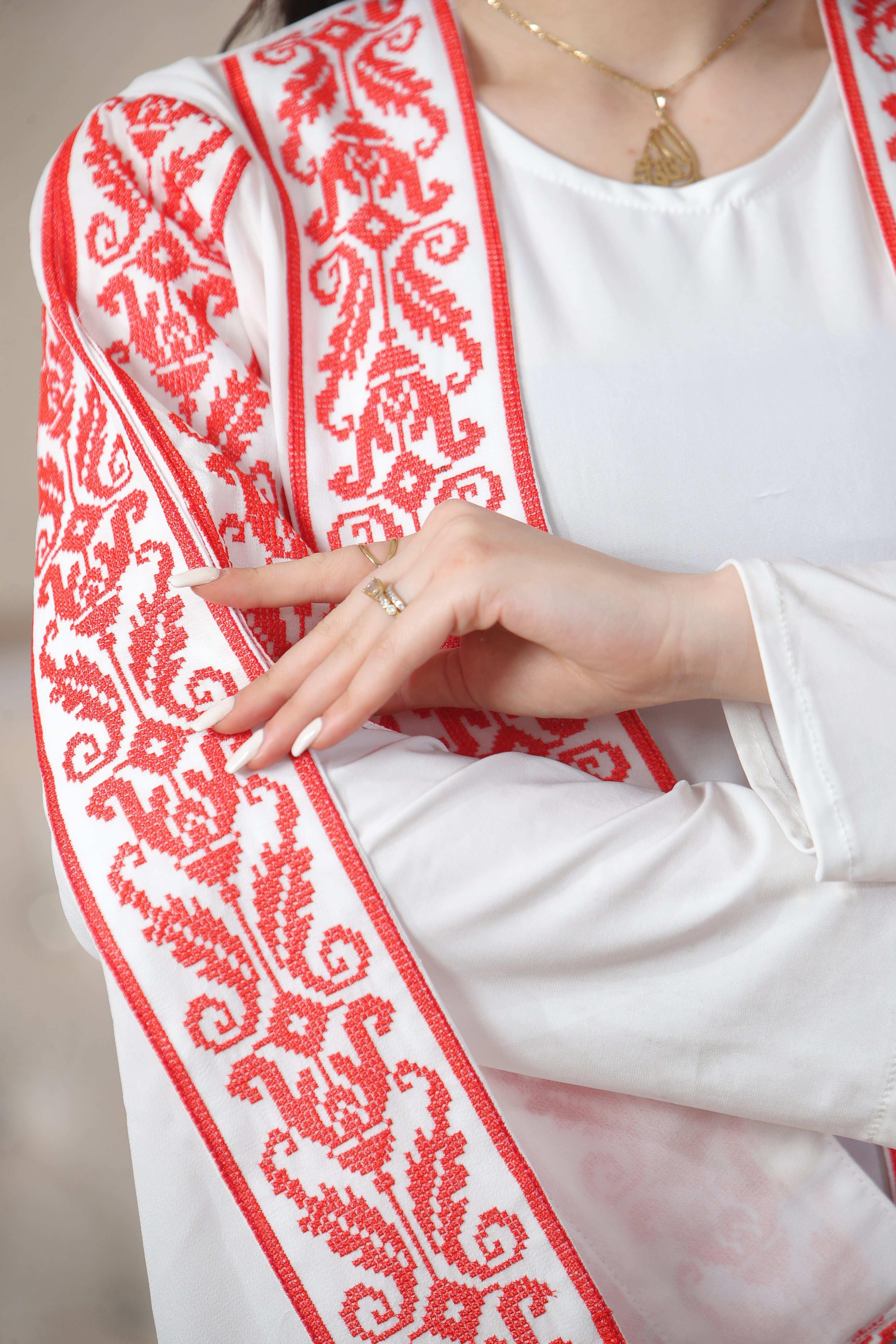 Close-up of Shereen Embroidered Bisht Abaya with red intricate embroidery on white fabric by Palestinian Elegance