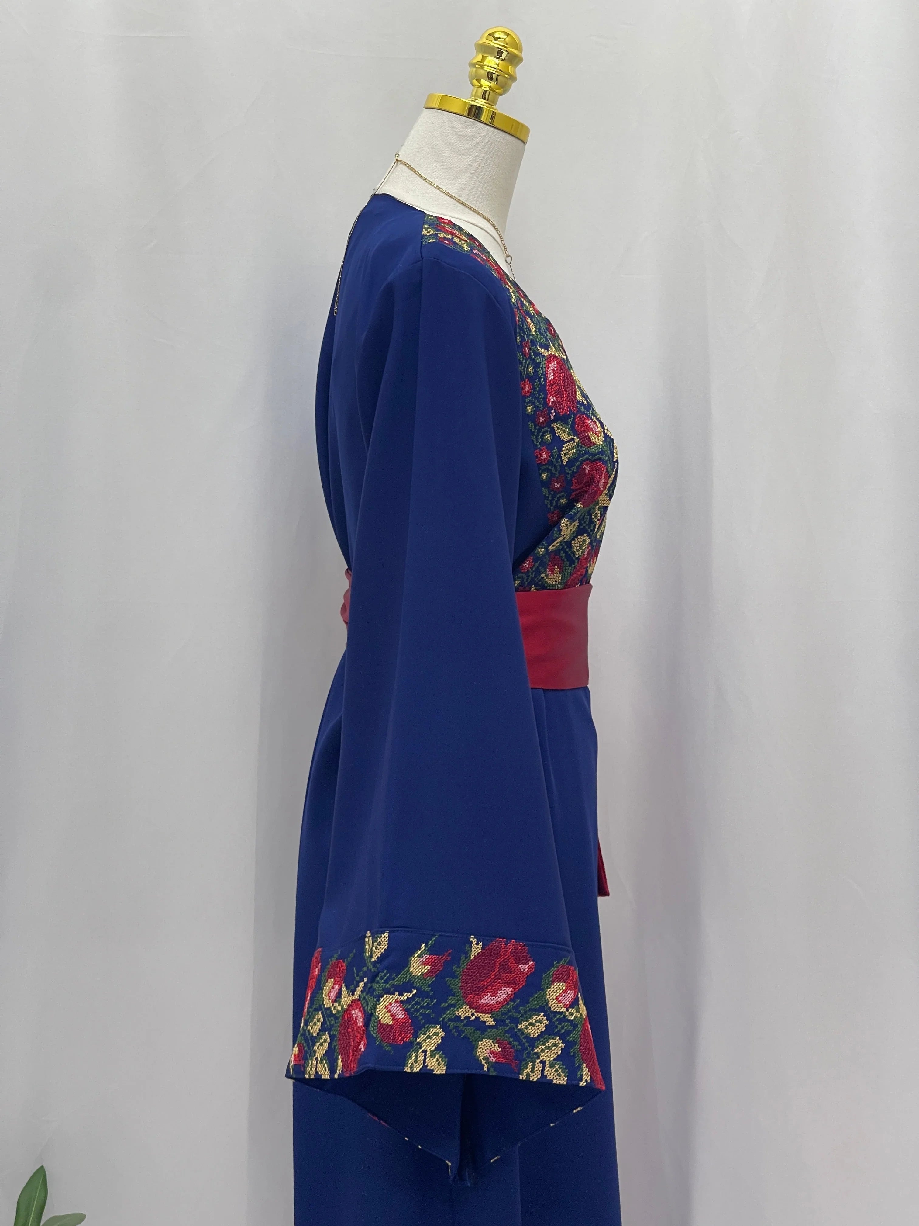 Blossom Royal Blue Thobe embroidered with red and pink floral panels and a red waist sash on mannequin