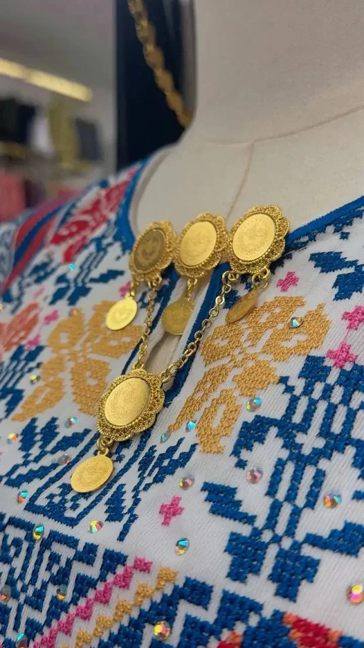 Palestinian Elegance imitated gold traditional gold brooch with ornate circular designs and hanging coins on embroidered fabric