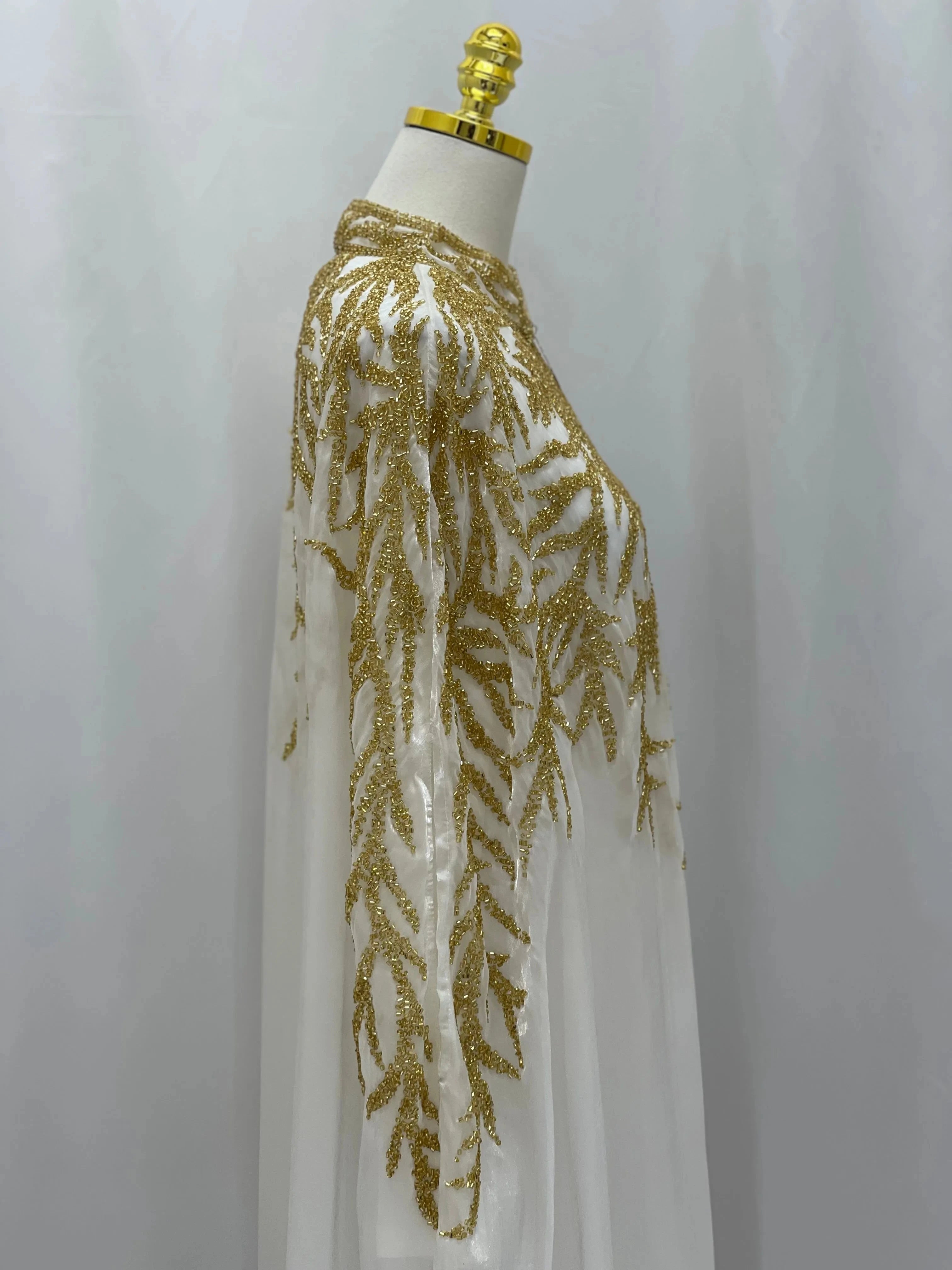 White traditional embroidery cape with intricate gold leaf patterns displayed on mannequin