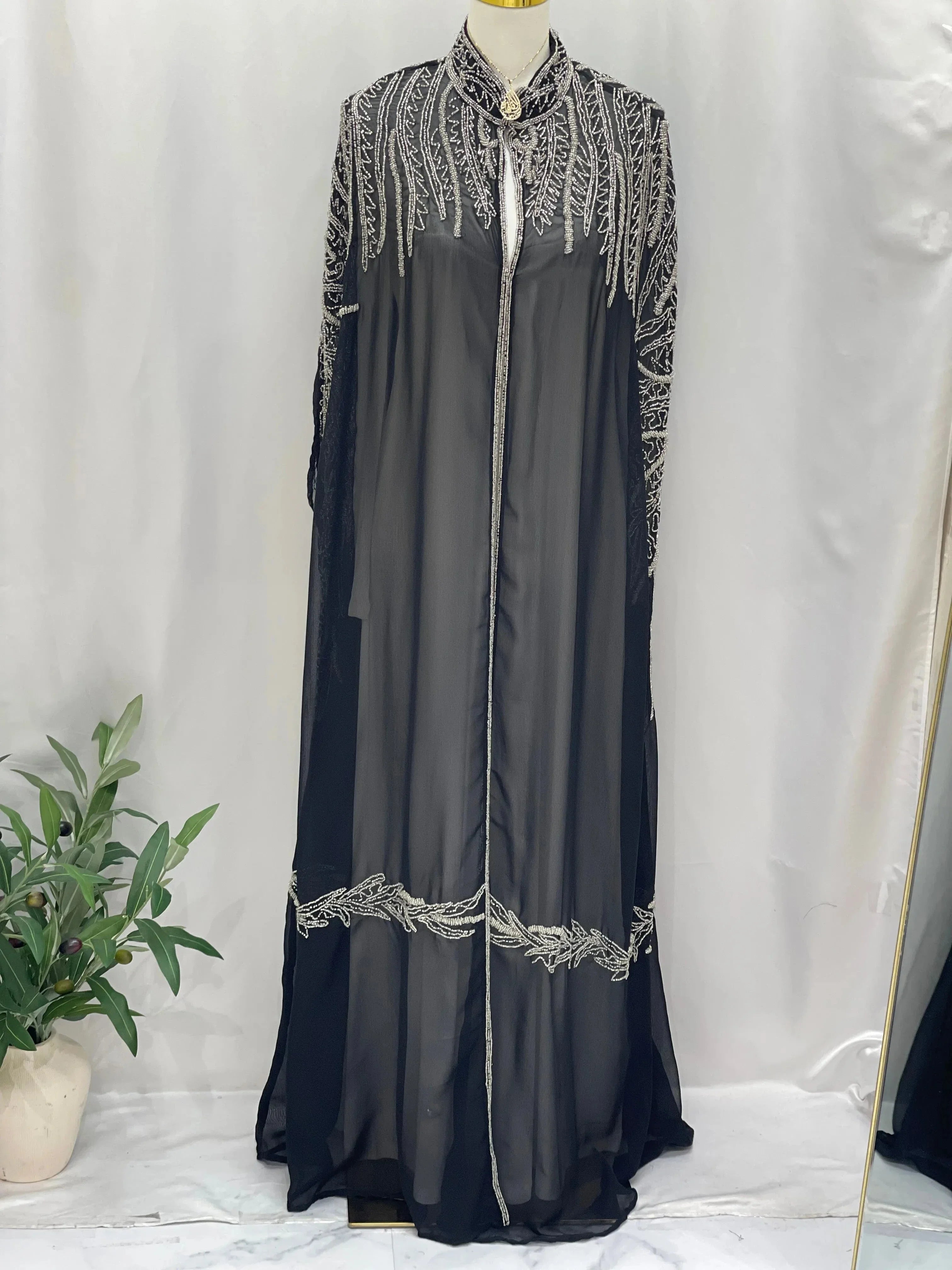Black traditional embroidery cape with intricate white designs from Palestinian Elegance displayed on a mannequin