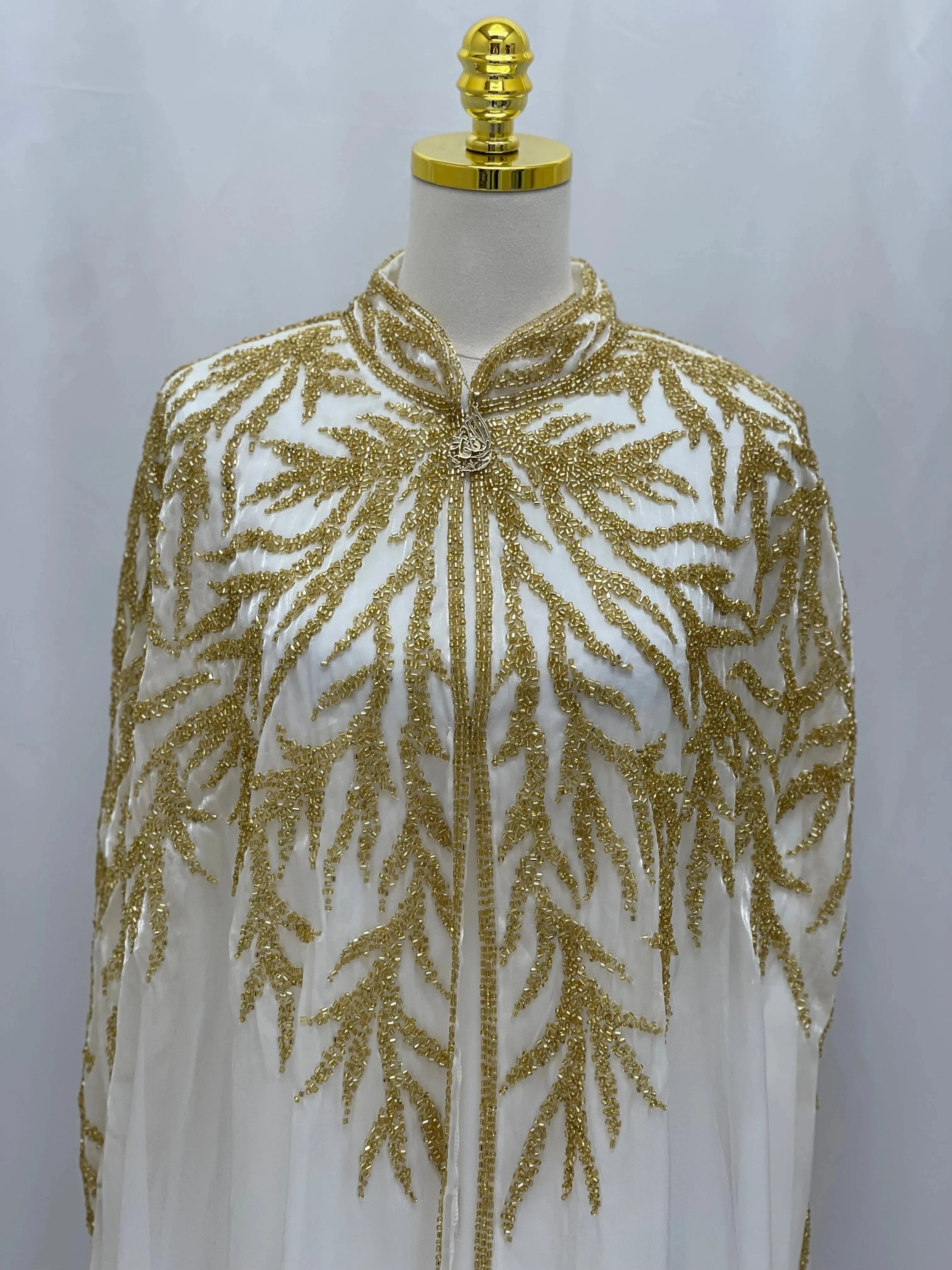 White traditional embroidery cape with intricate gold leaf patterns by Palestinian Elegance
