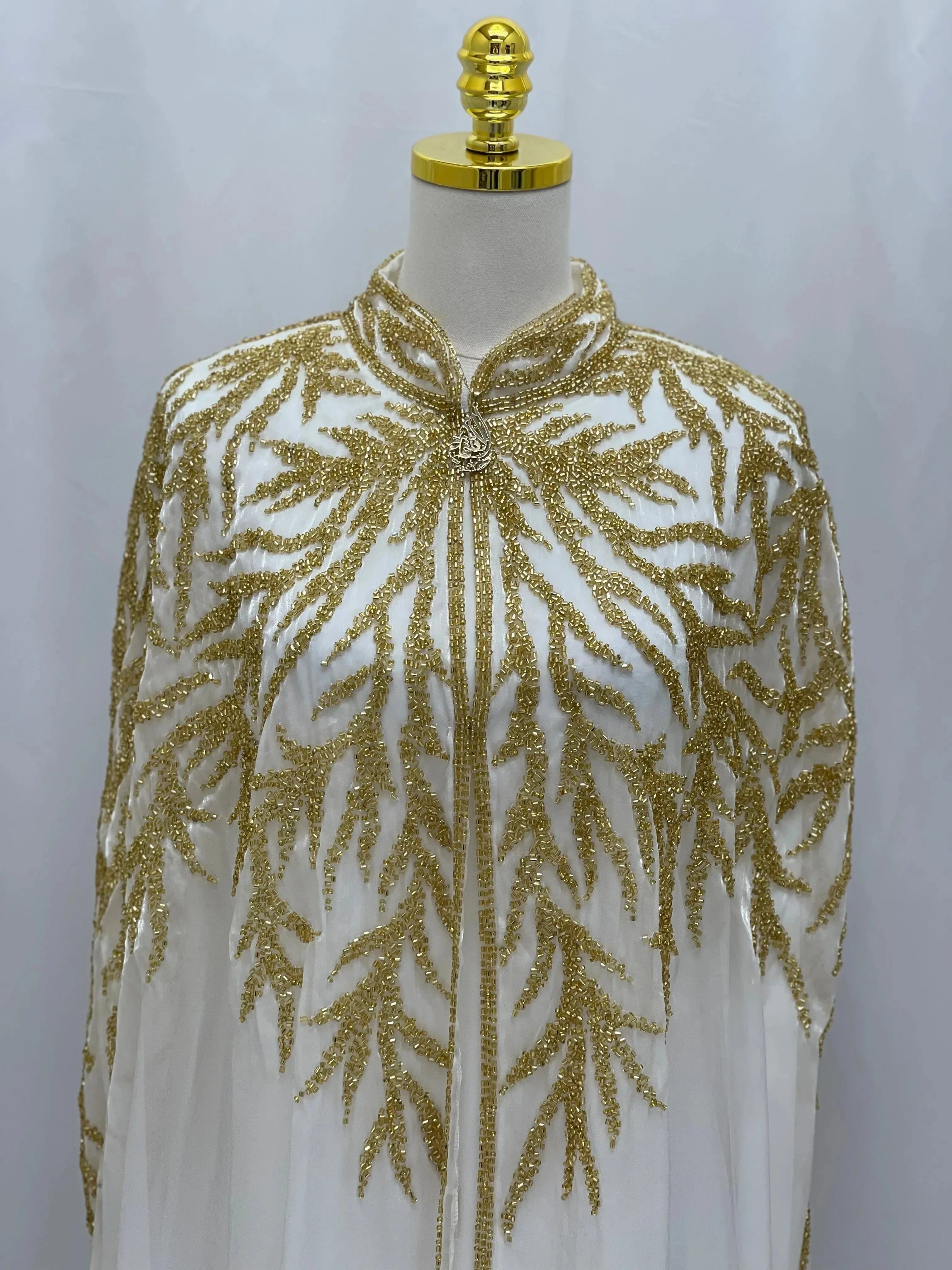 White traditional embroidery cape with intricate gold leaf patterns by Palestinian Elegance
