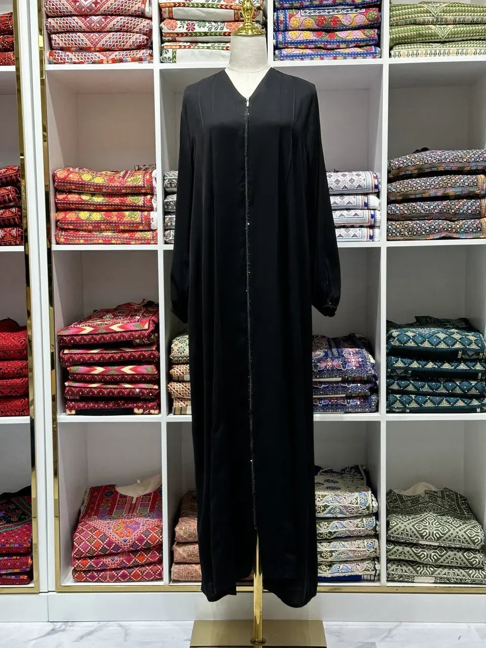 Palestinian Elegance black abaya simple design displayed on mannequin in front of shelves with colorful folded fabrics
