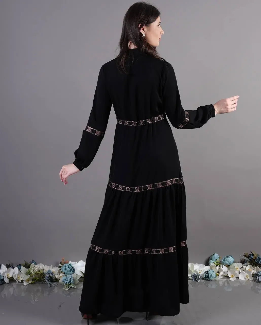 Palestinian Elegance black elegant abaya dress with decorative trim worn by woman standing against gray background