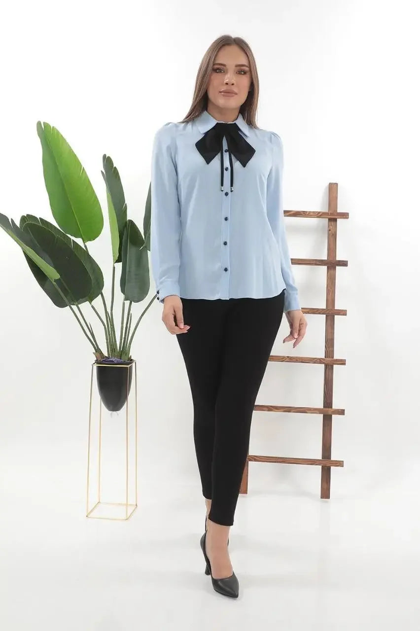 Woman wearing elegant bow tie blouse in light blue with black bow and black pants by Palestinian Elegance