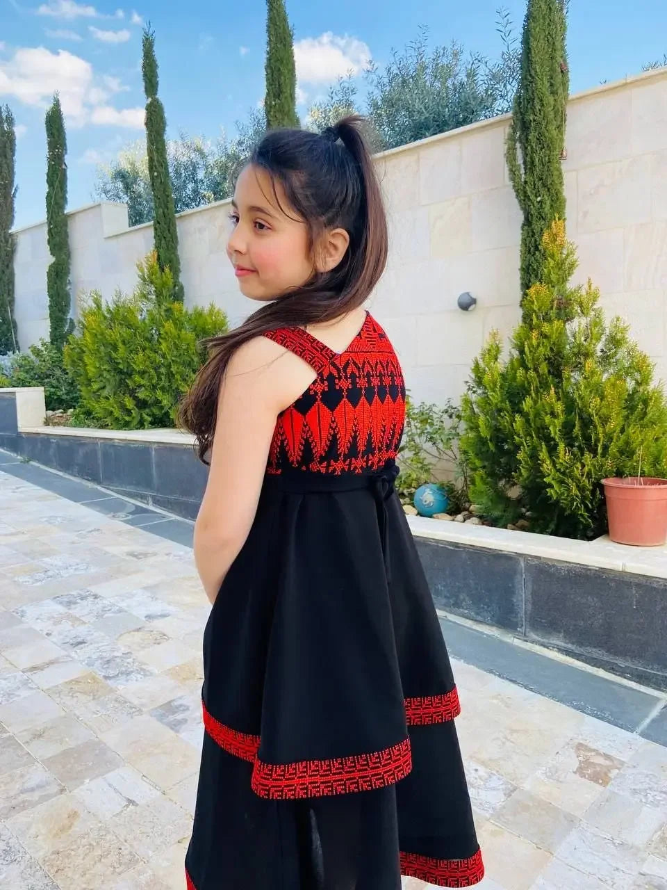 Girl wearing embroidered dress for kids in black and red by Palestinian Elegance outdoors