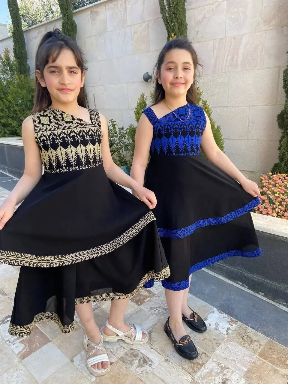 Girls wearing Palestinian Elegance embroidered dress for kids in black with traditional blue and beige patterns