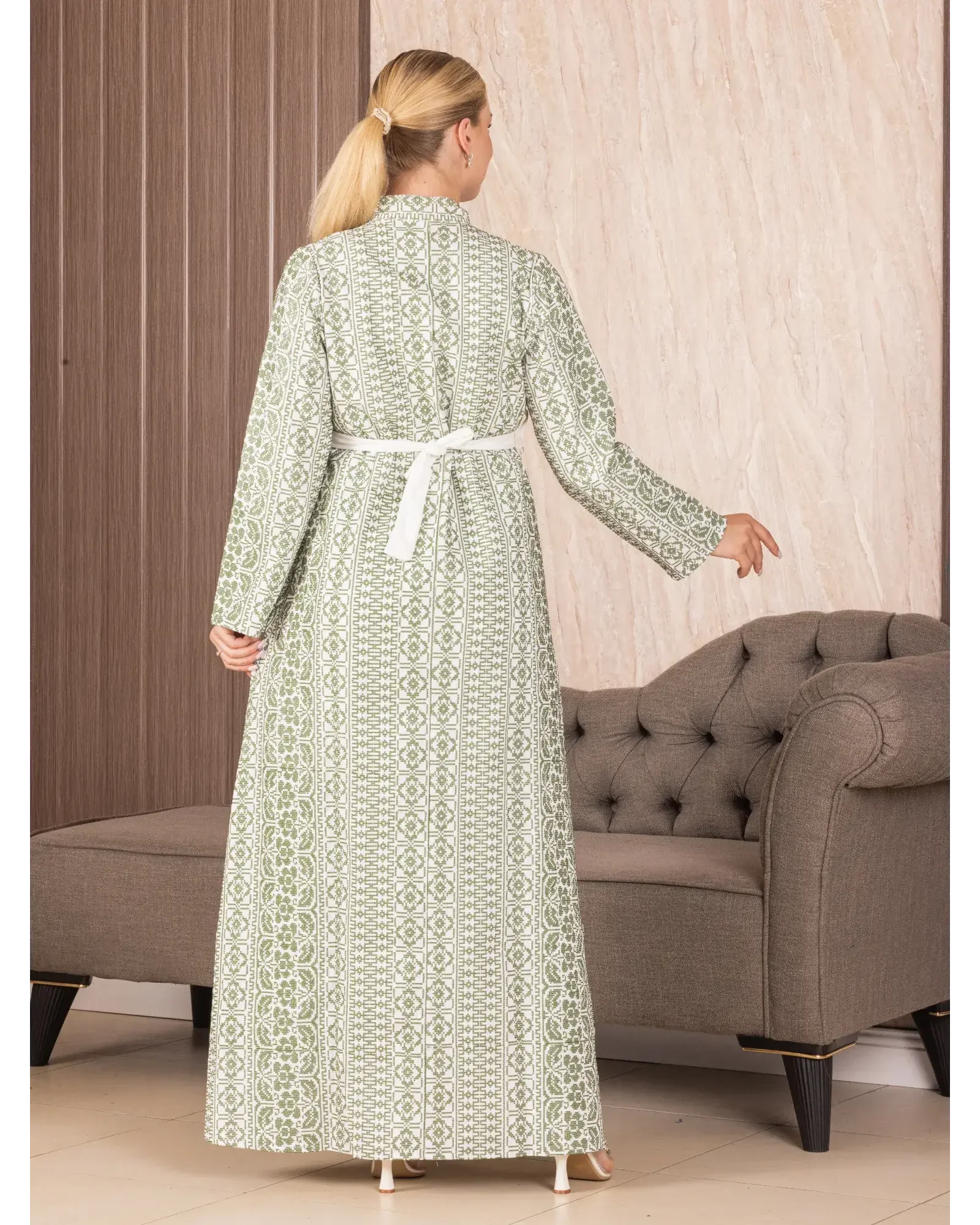 Back view of a woman wearing a Palestinian Elegance embroidered long cardigan with white belt and green traditional patterns