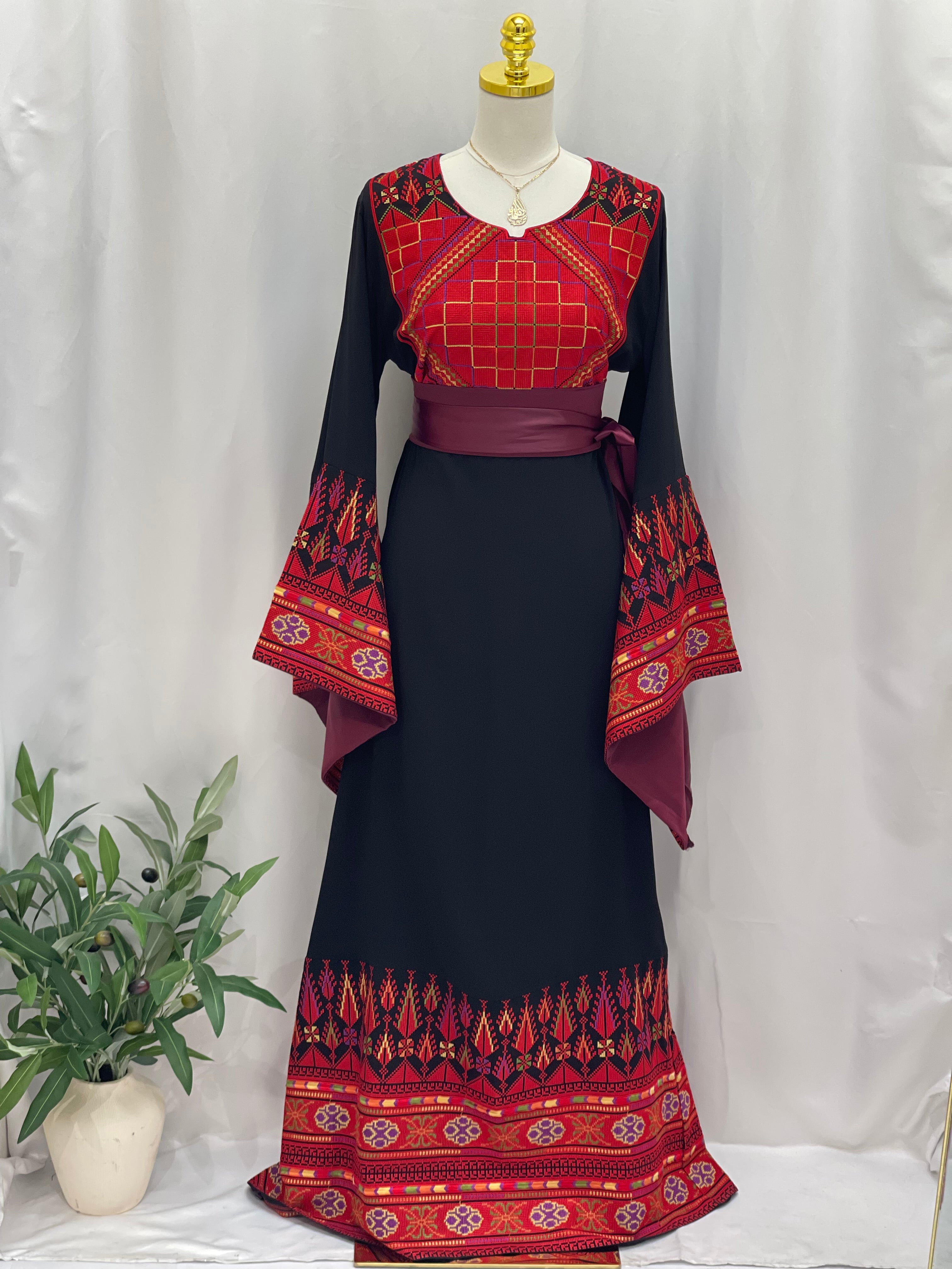 Embroidered Palestinian thoub dress with red geometric and floral patterns on black fabric by Palestinian Elegance