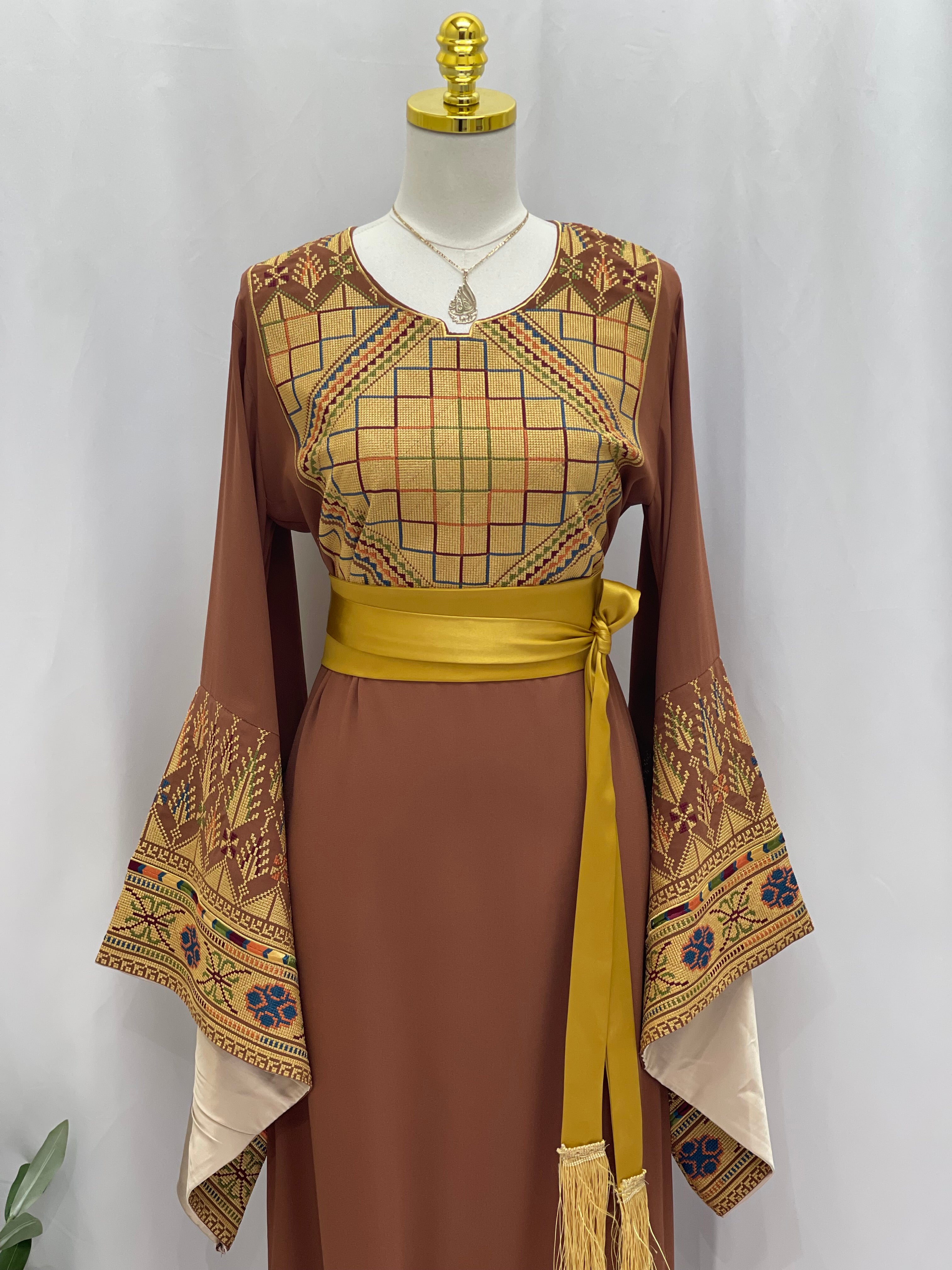 Embroidered Palestinian thoub dress by Palestinian Elegance with geometric and floral patterns and a yellow sash belt