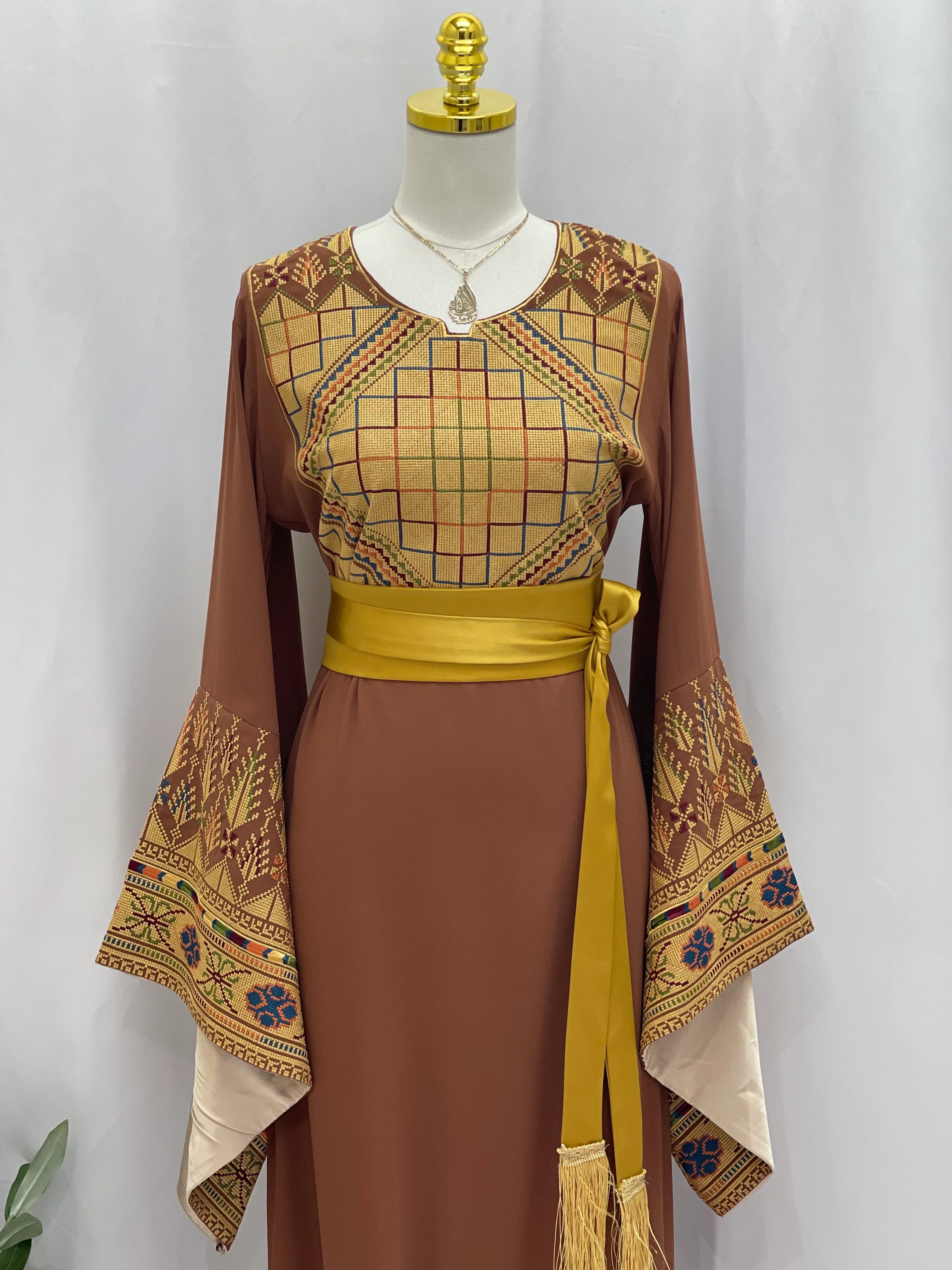 Embroidered Palestinian thoub dress by Palestinian Elegance with geometric and floral patterns and a yellow sash belt