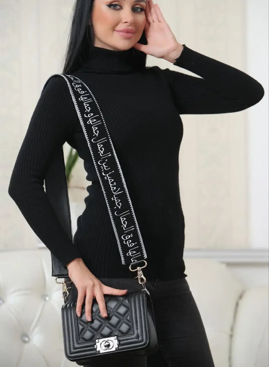 Black embroidered purse with poetic strap featuring Arabic calligraphy carried by woman in black sweater