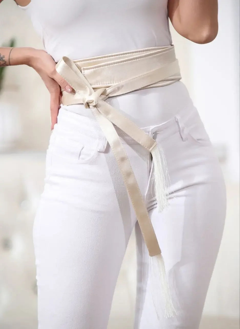 Woman wearing an embroidered satin belt tied around the waist over white pants