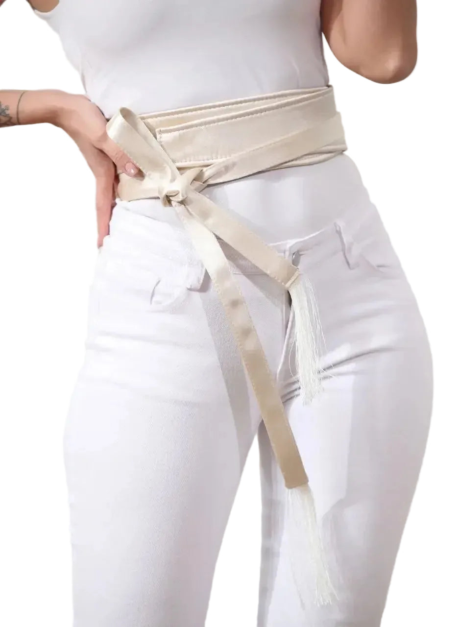 Woman wearing an embroidered satin belt tied around the waist over white pants