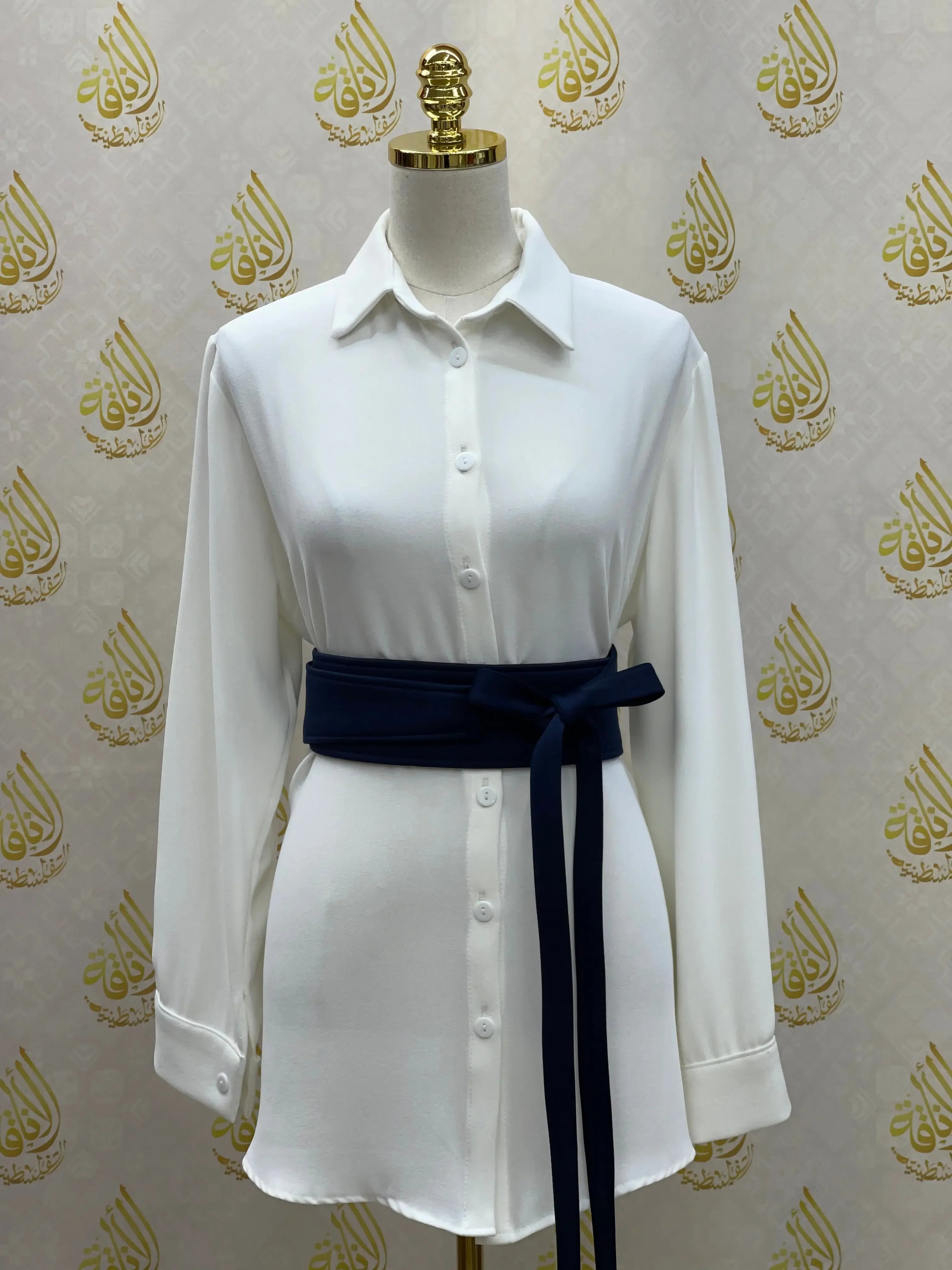 White button-up shirtdress styled with a navy embroidered satin belt by Palestinian Elegance