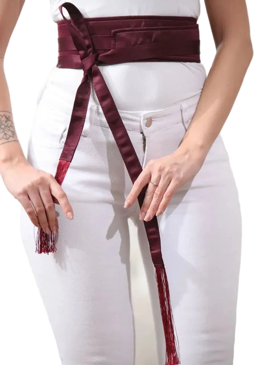 Maroon embroidered satin belt with tassels tied around waist over white pants