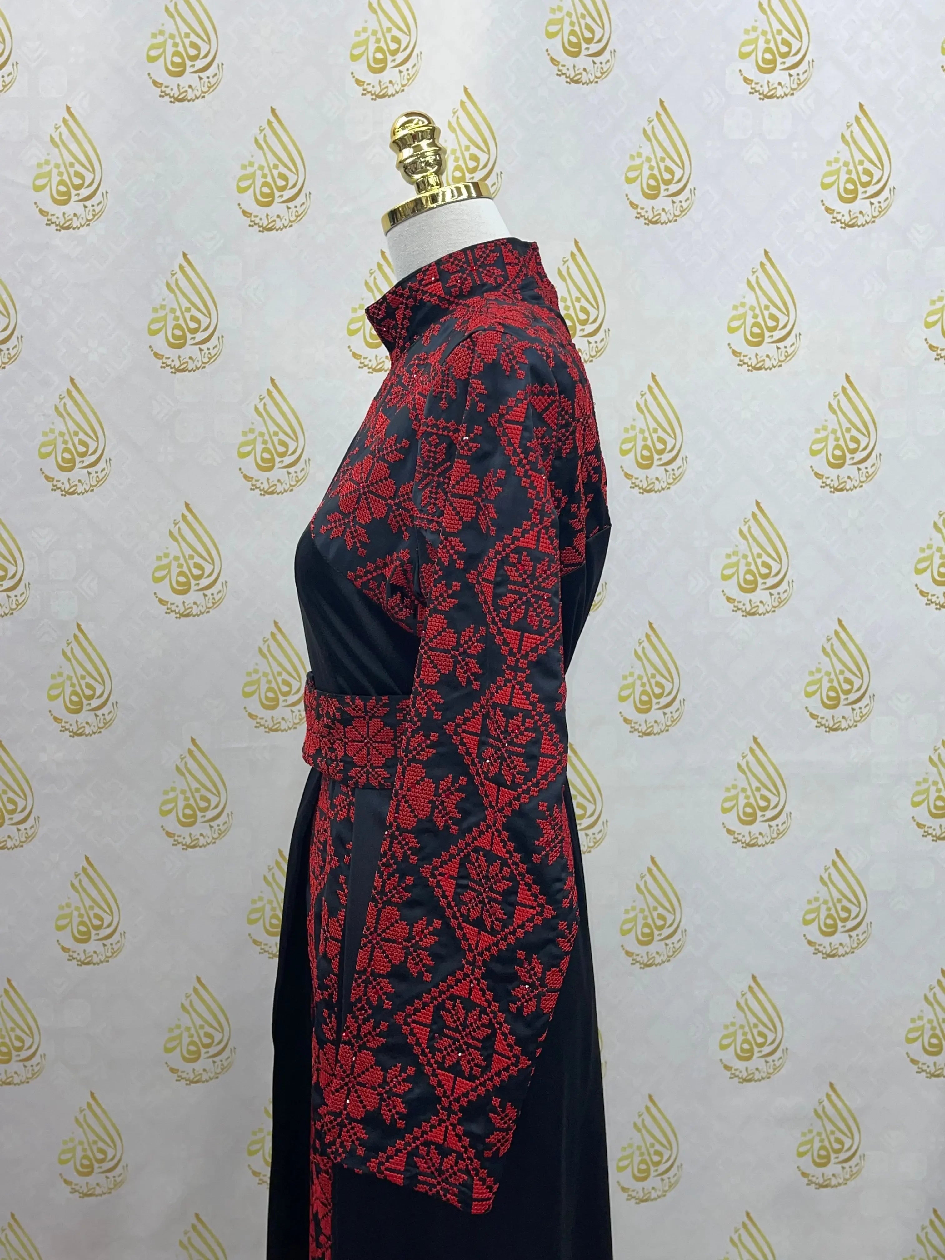 Palestinian Elegance embroidered satin dress with intricate red floral patterns on black fabric, displayed on mannequin