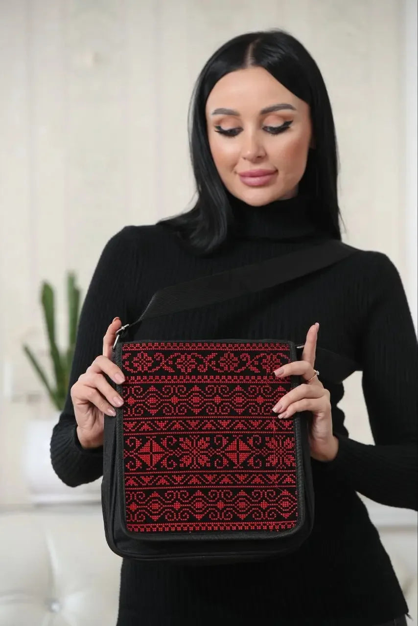 Palestinian Elegance embroidered shoulder bag with traditional red and black patterns held by a woman in black outfit