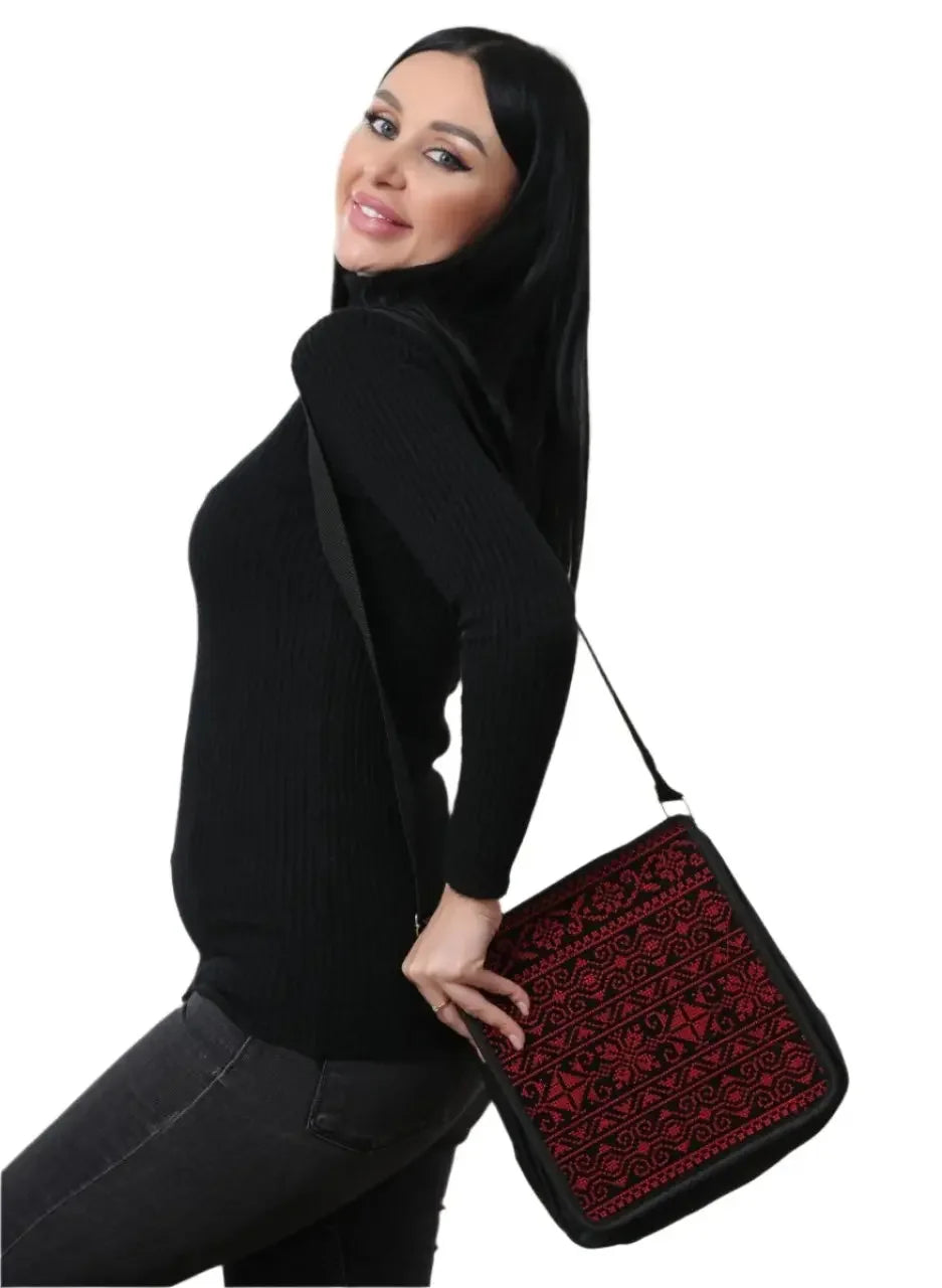 Woman wearing a black sweater carrying a Palestinian Elegance embroidered shoulder bag with red and black geometric patterns