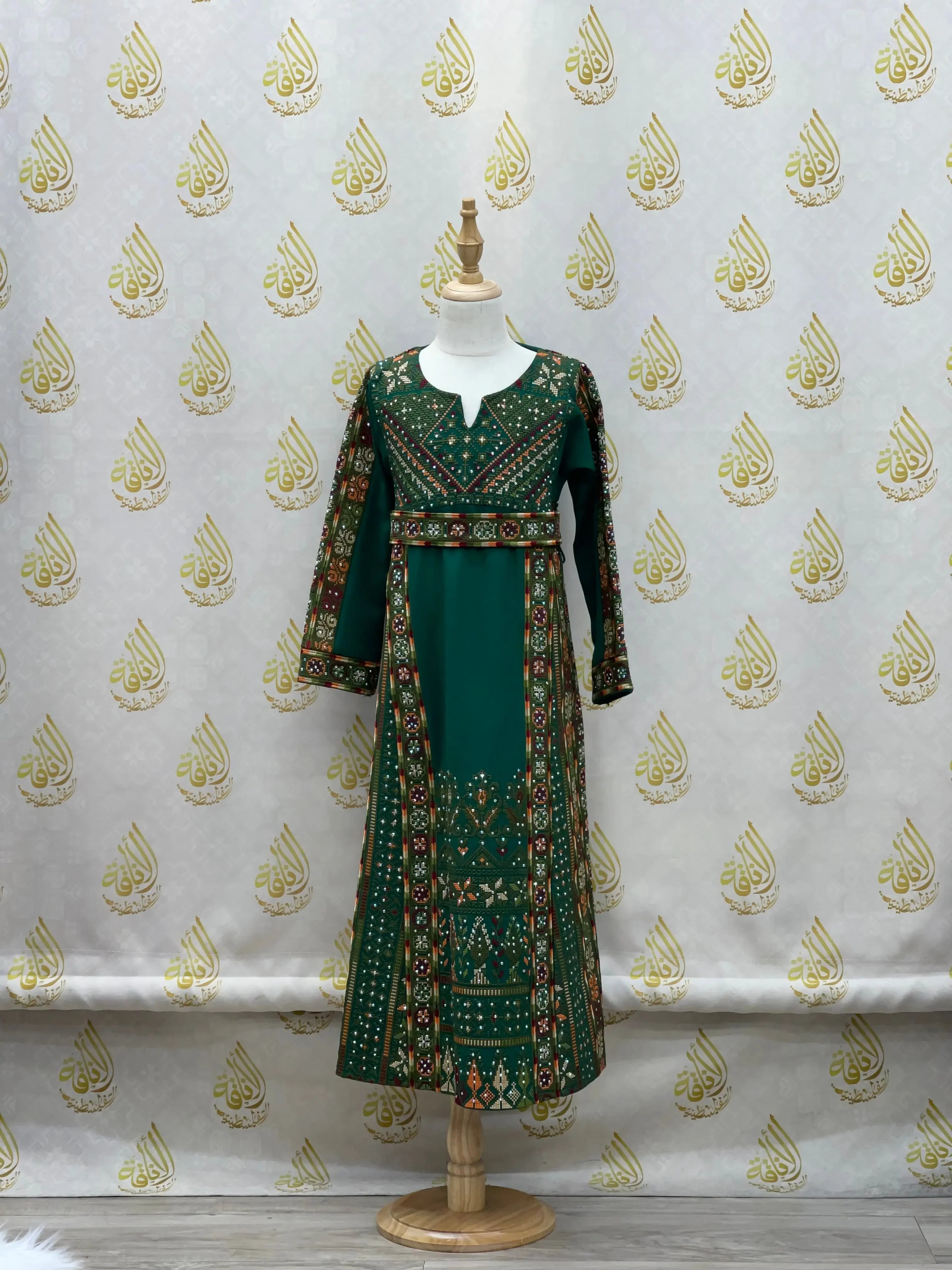 Green embroidered thoub for girls with intricate traditional Palestinian designs on a mannequin