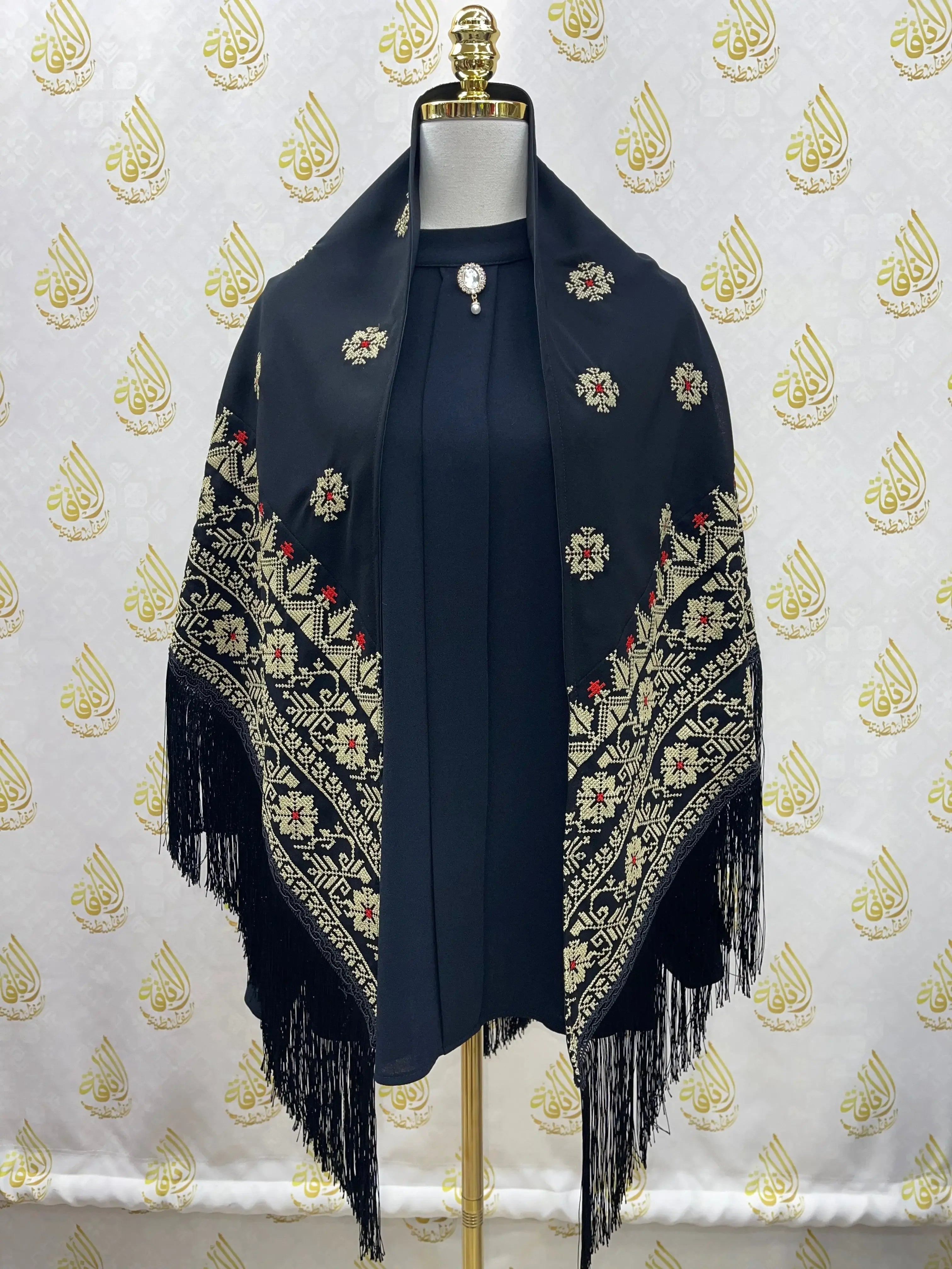 Black embroidered triangle shawl with floral patterns and fringe detailing by Palestinian Elegance