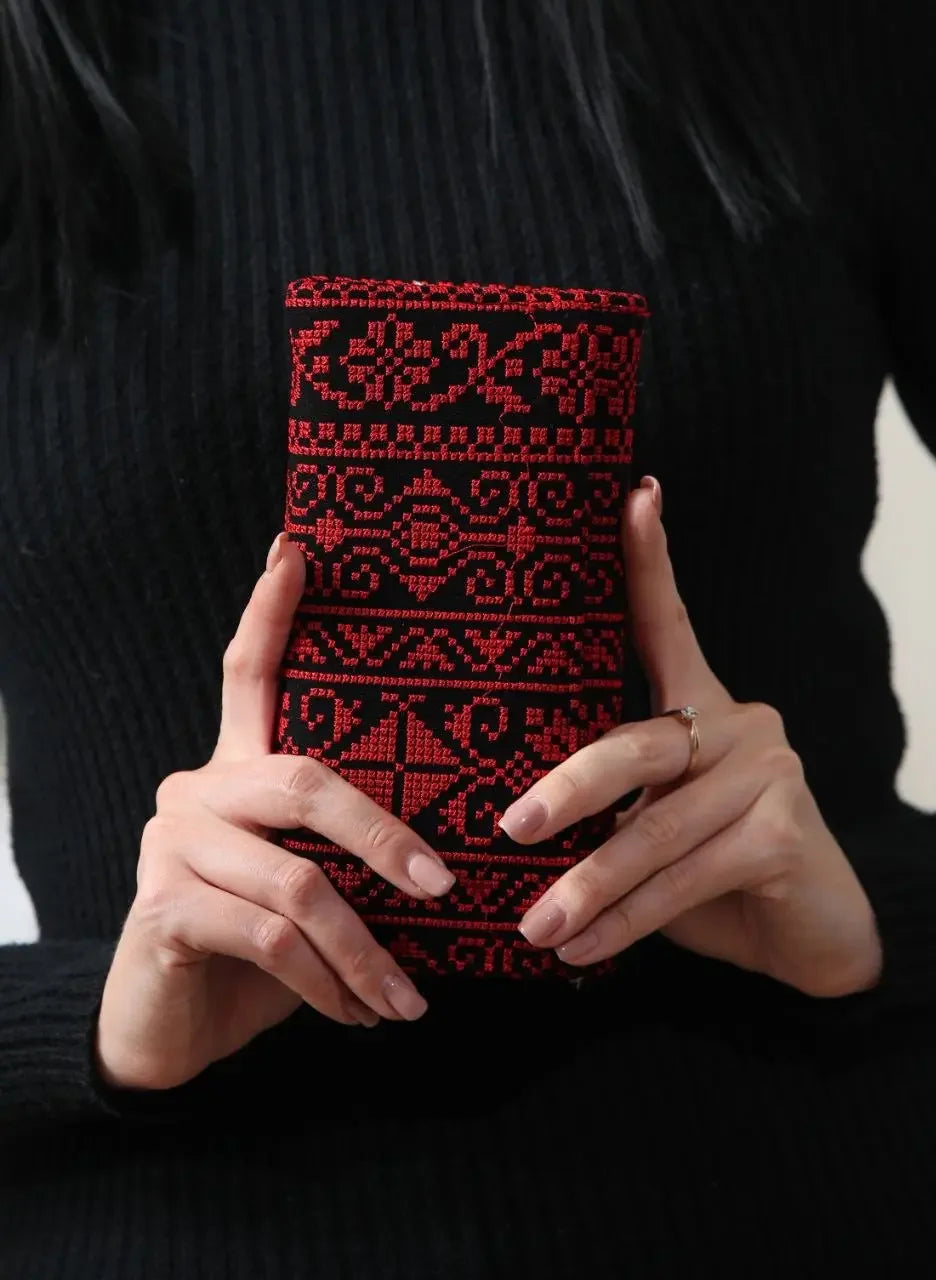 Palestinian Elegance embroidered wallet for women in black and red held by woman wearing black sweater