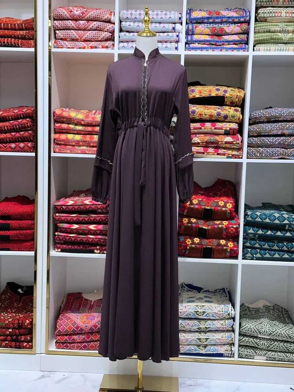 Palestinian Elegance fancy abaya dress for women in dark purple displayed on mannequin with colorful fabric shelves