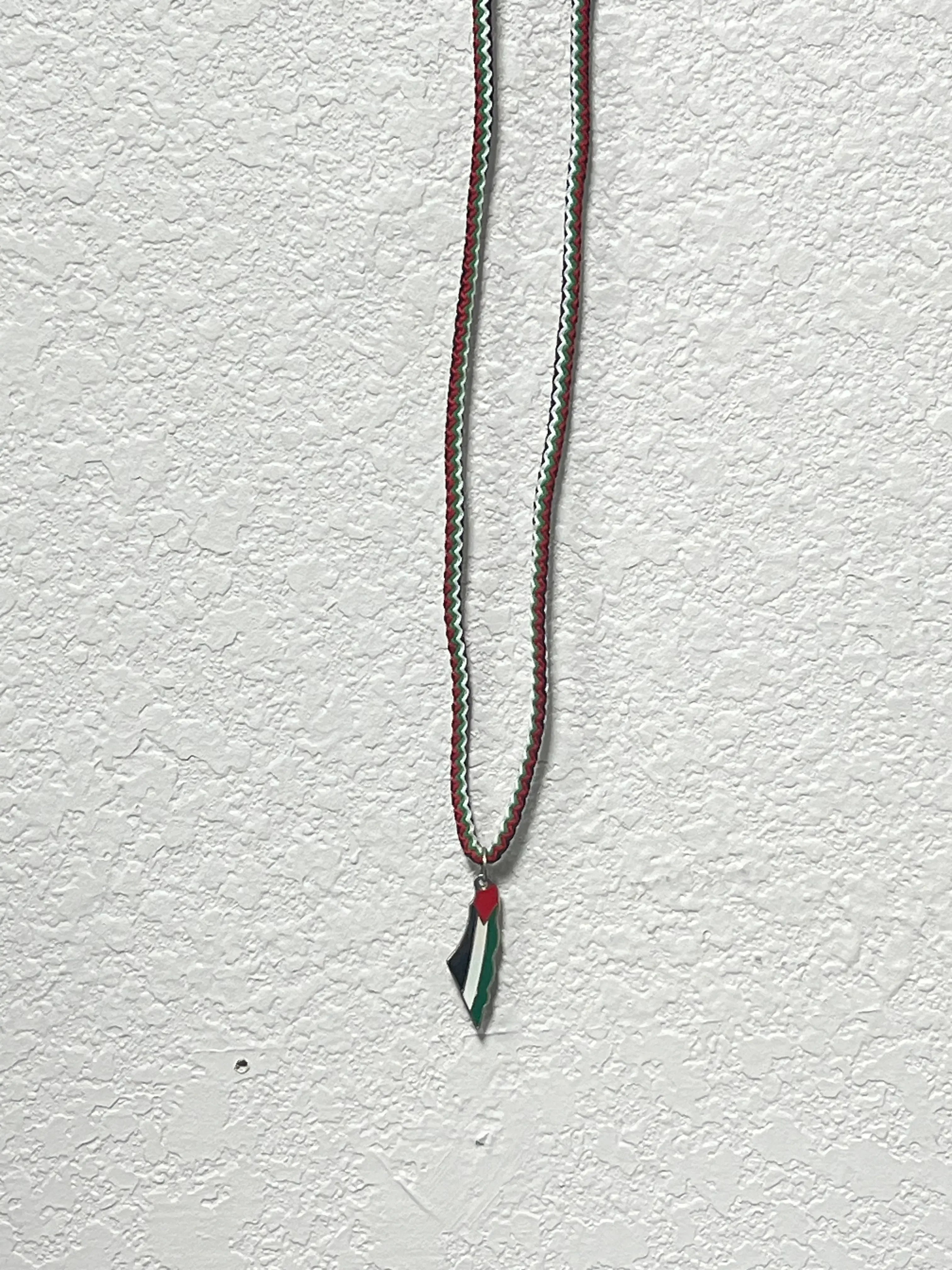 Handmade Palestinian silver necklace with red, black, white, and green pendant on textured white background