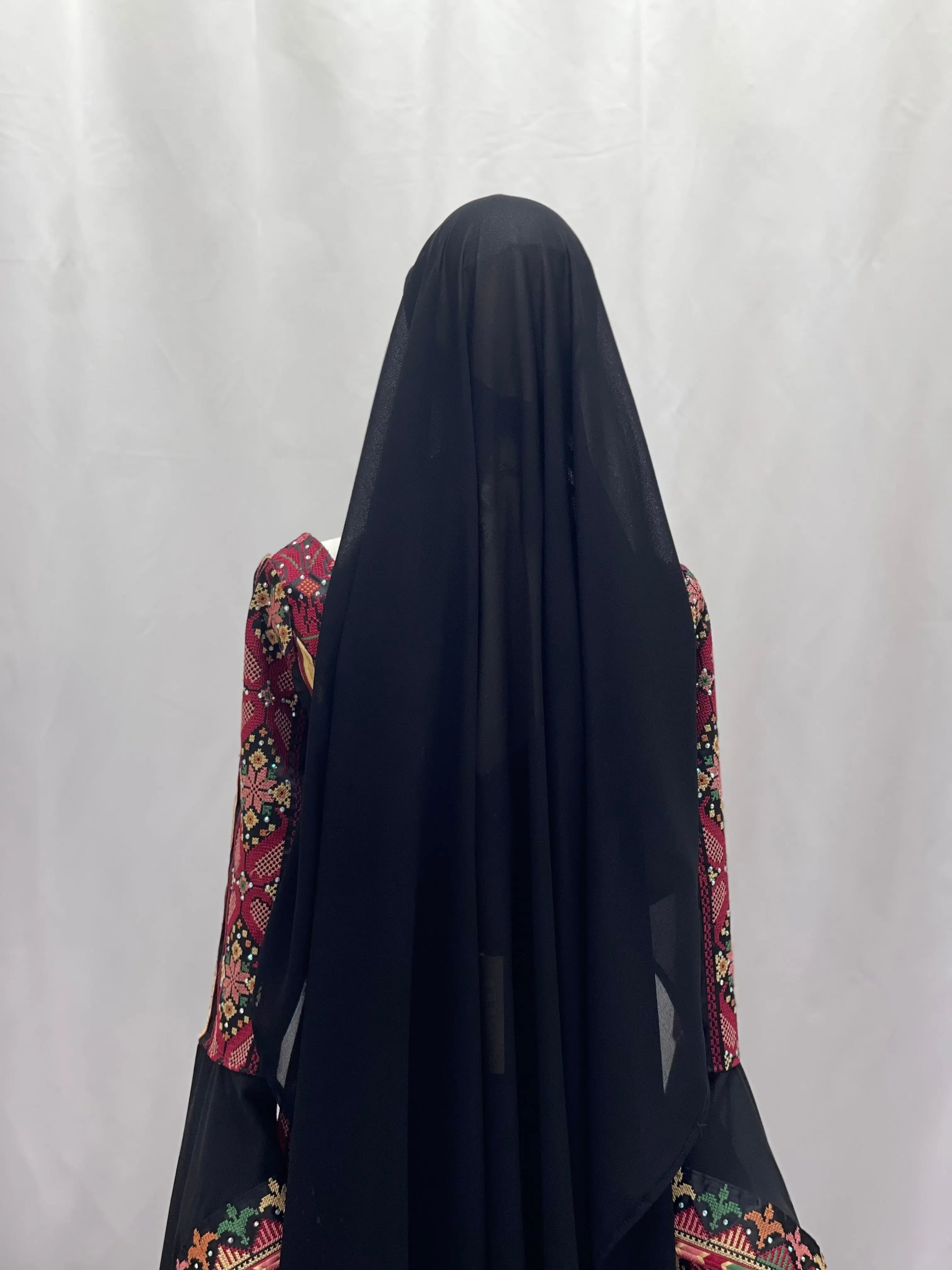 Traditional Palestinian khirka with gold coins featuring intricate embroidery and black fabric draped over the back