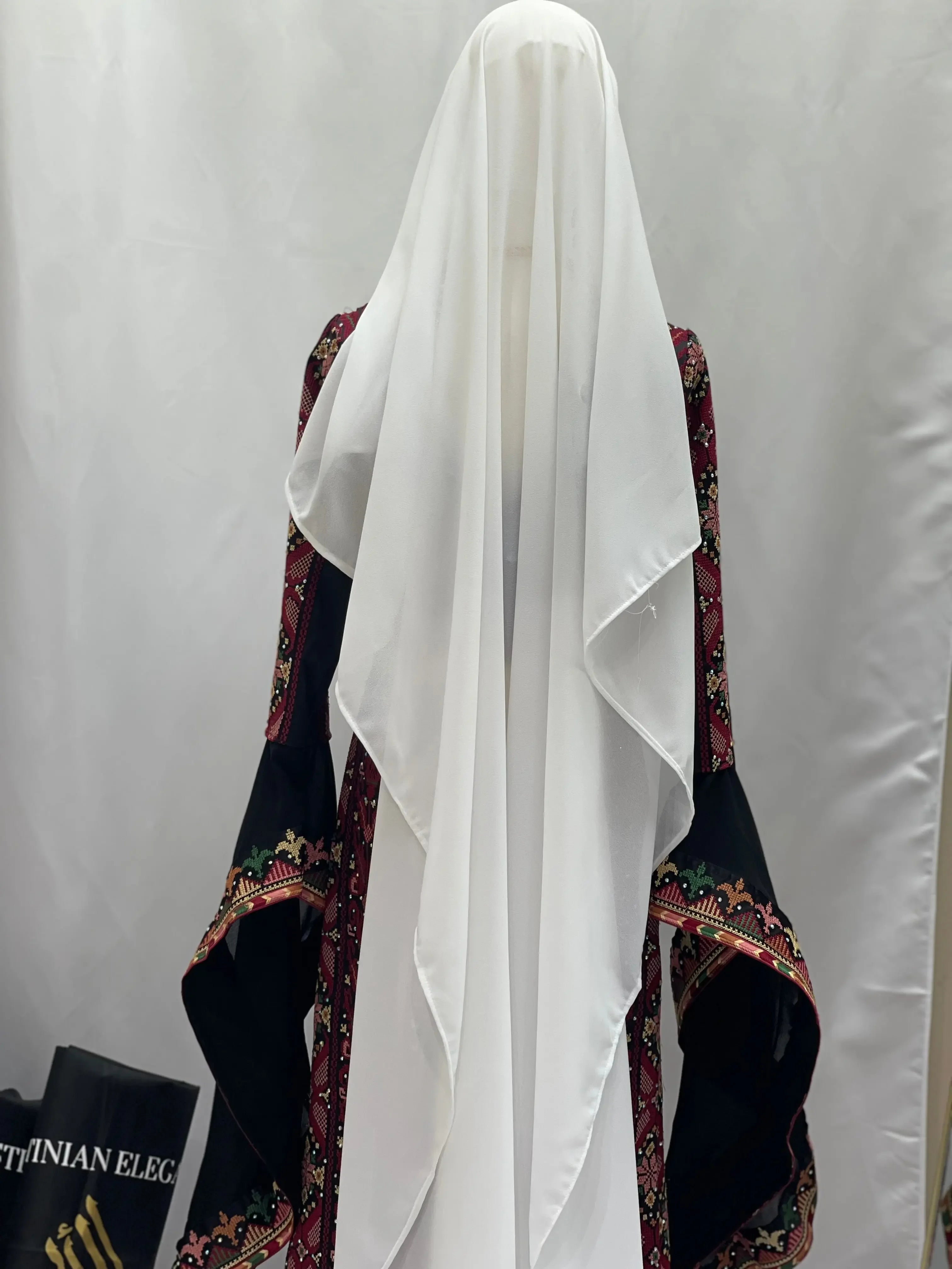 Palestinian Elegance khirka with gold coins featuring traditional embroidered black and red fabric with white veil accessory