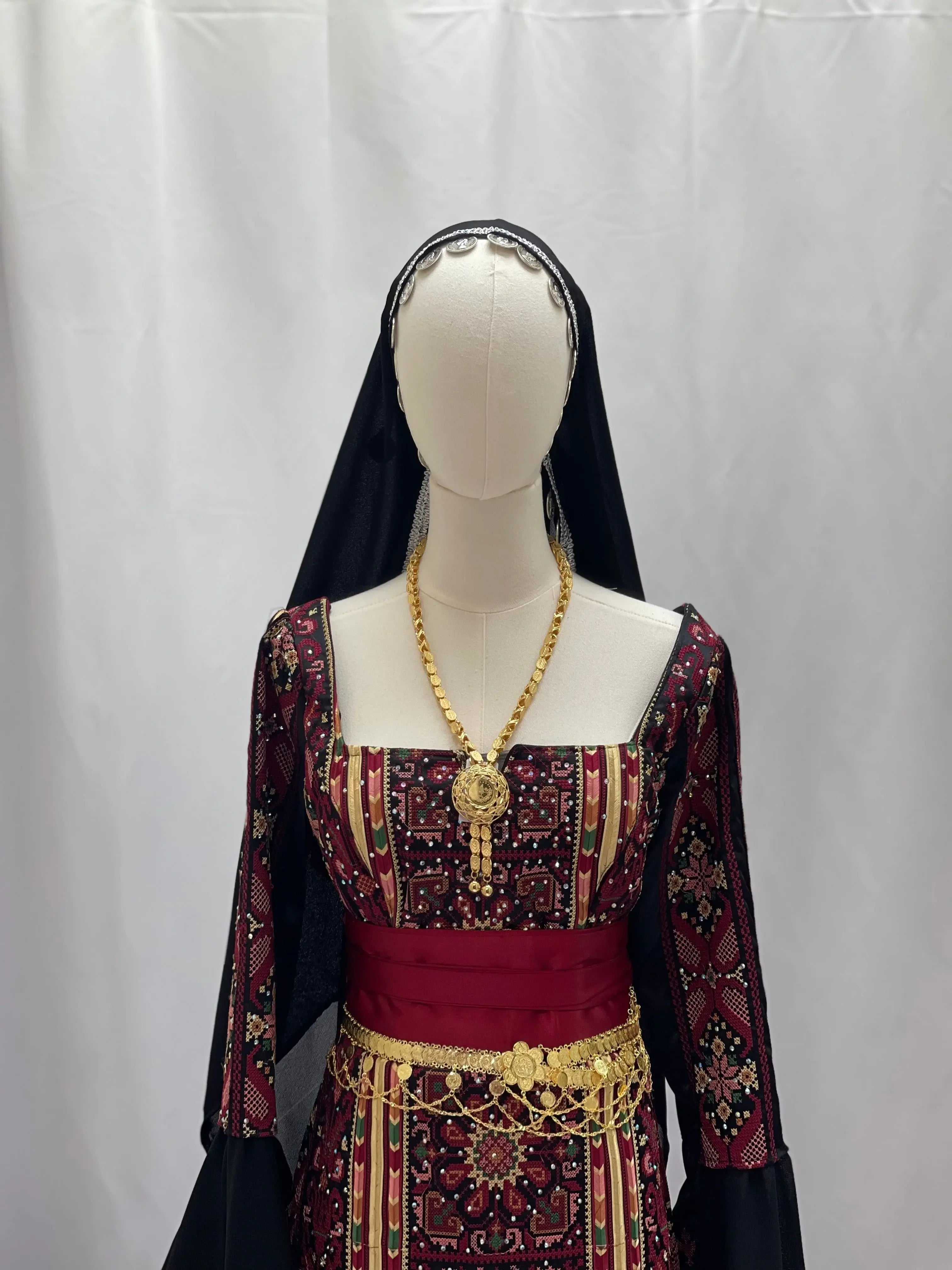Traditional Palestinian khirka with gold coins accessory worn over embroidered dress with black headscarf