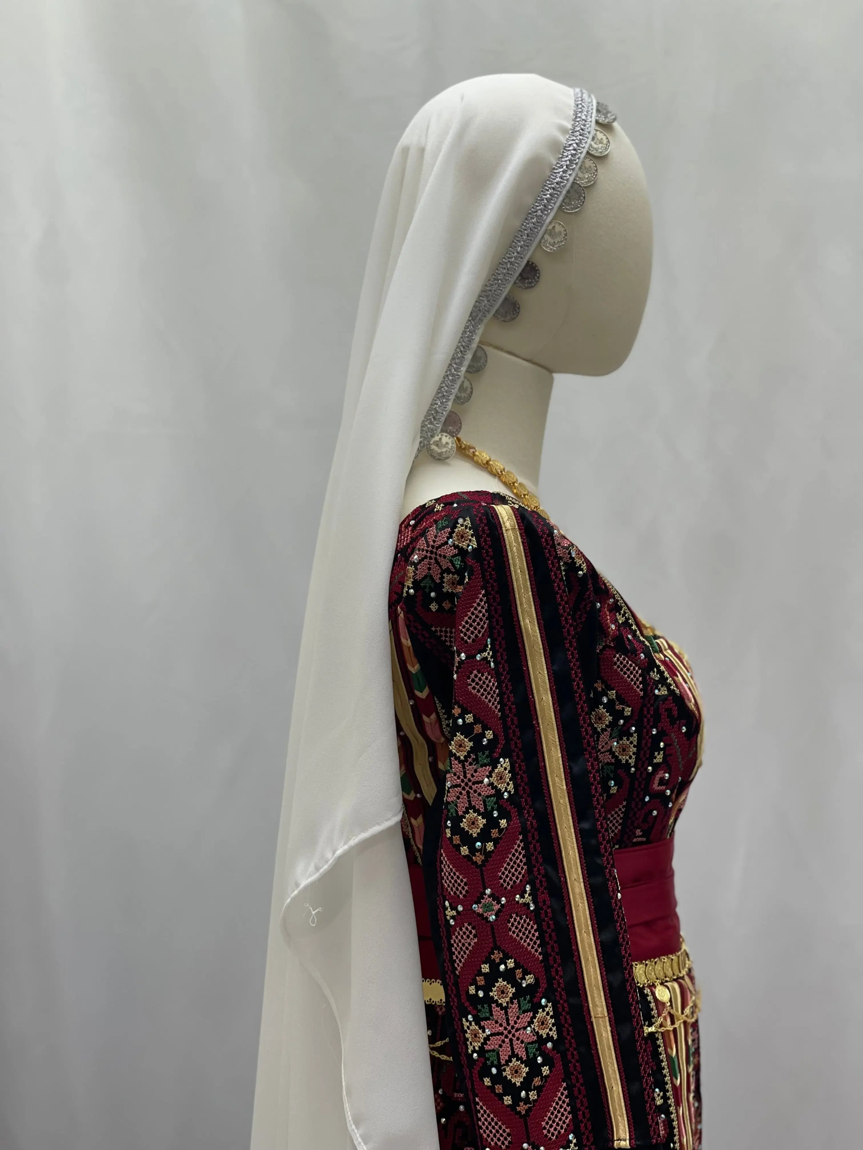 Palestinian Elegance khirka with gold coins on a mannequin featuring traditional embroidery and white headscarf