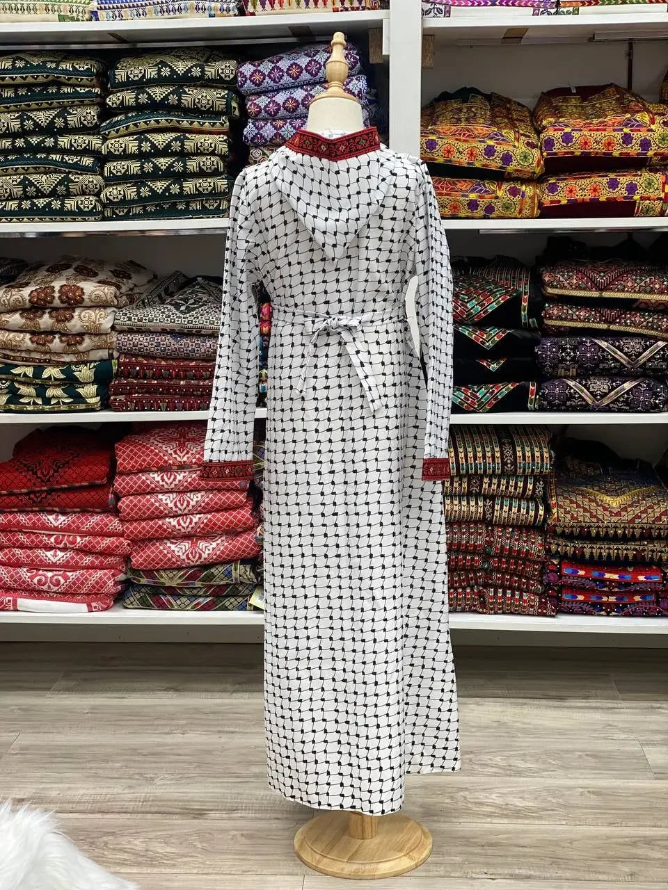 Kids embroidered bisht in white with black and red accents displayed on a mannequin by Palestinian Elegance