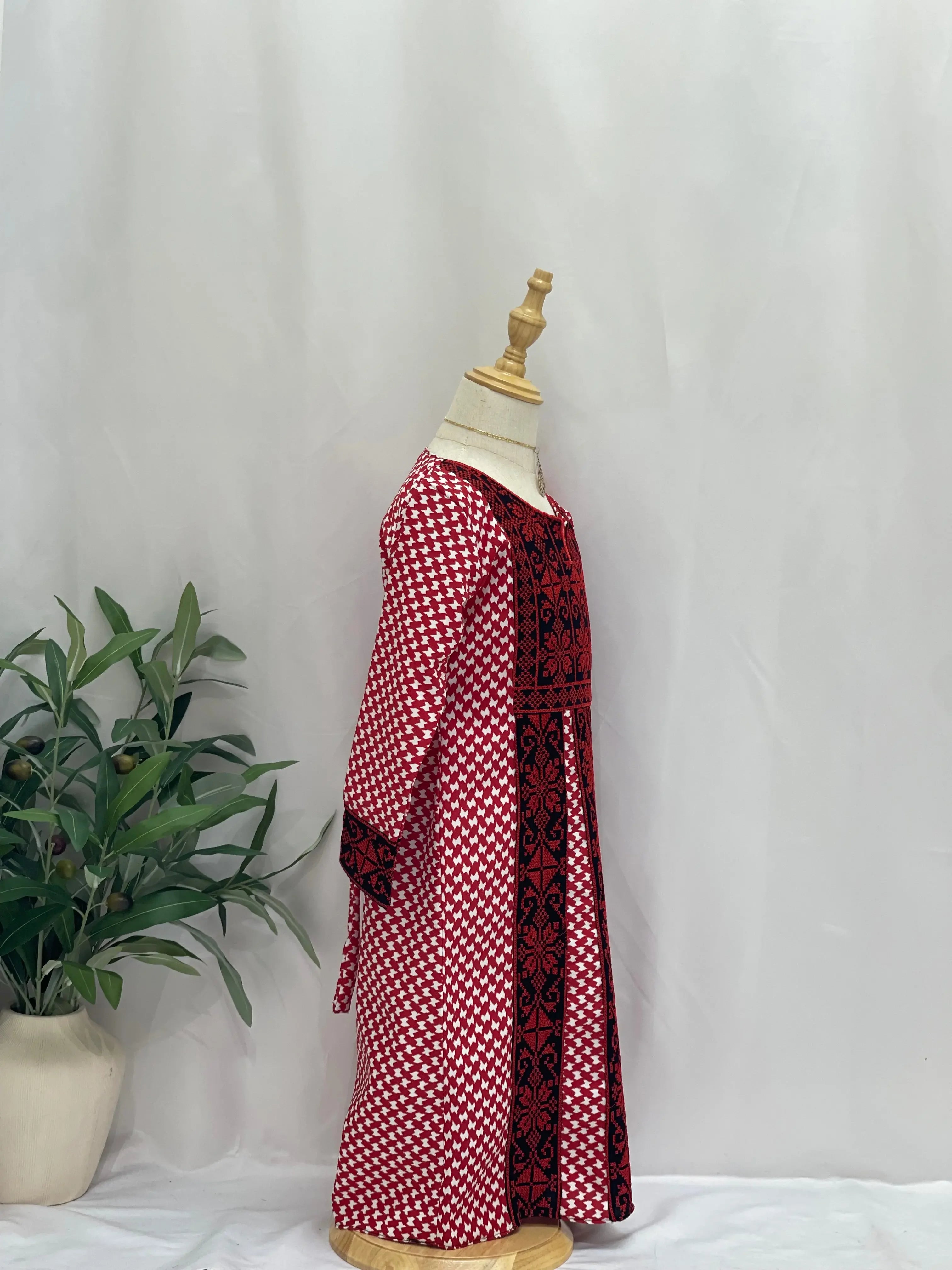 Kids embroidered Palestinian dress in red and black with traditional patterns displayed on a mannequin