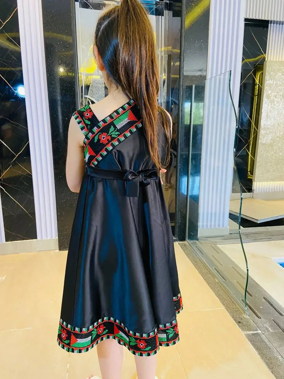 Young girl wearing a black kids Palestine dress with traditional red and green embroidery details