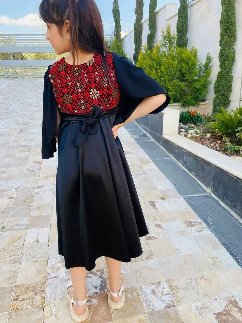 Young girl wearing a black kids tatreez dress with red embroidered traditional Palestinian design