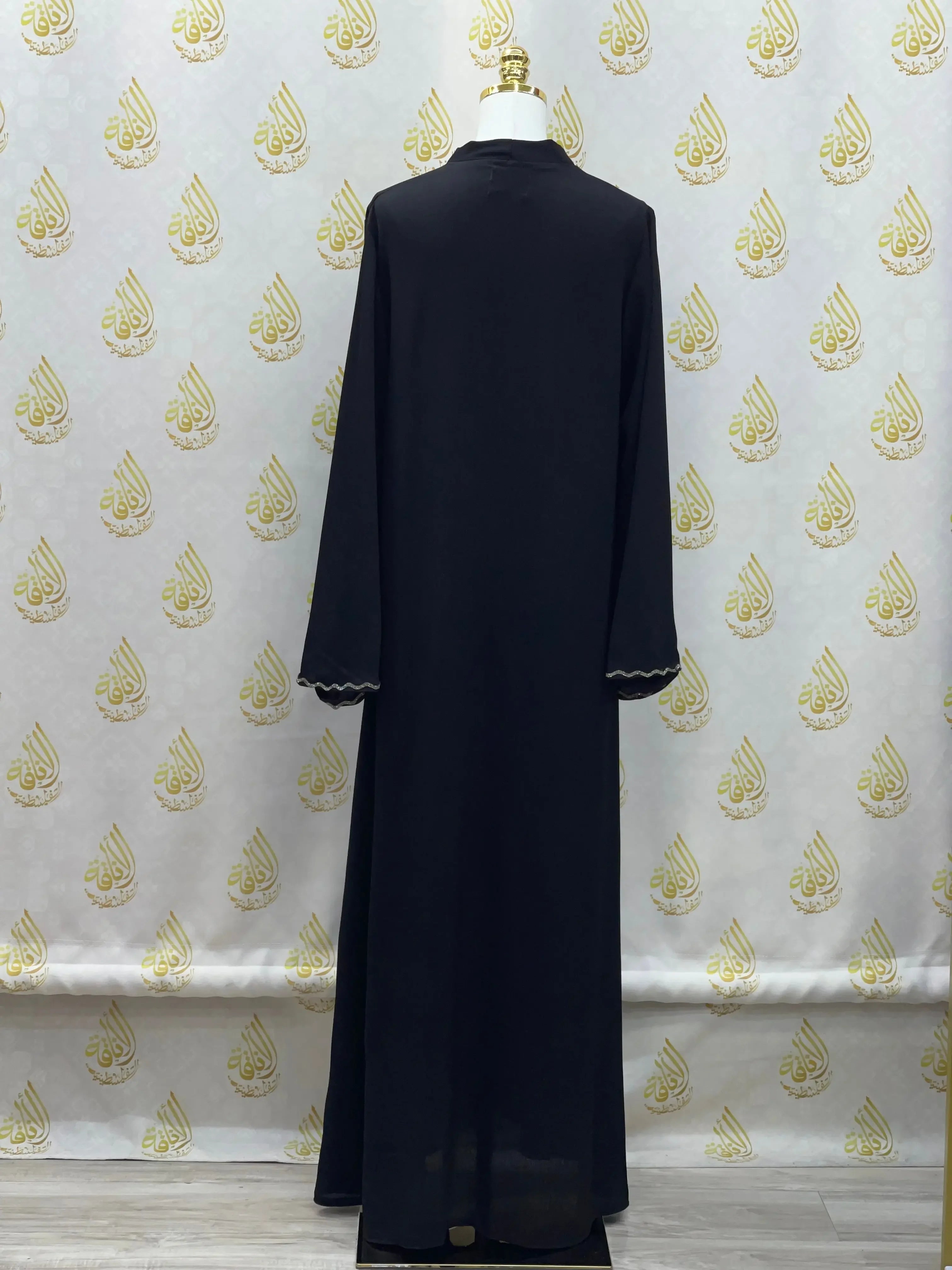 Black luxurious cloche cut abaya from Palestinian Elegance displayed on a mannequin against decorative backdrop