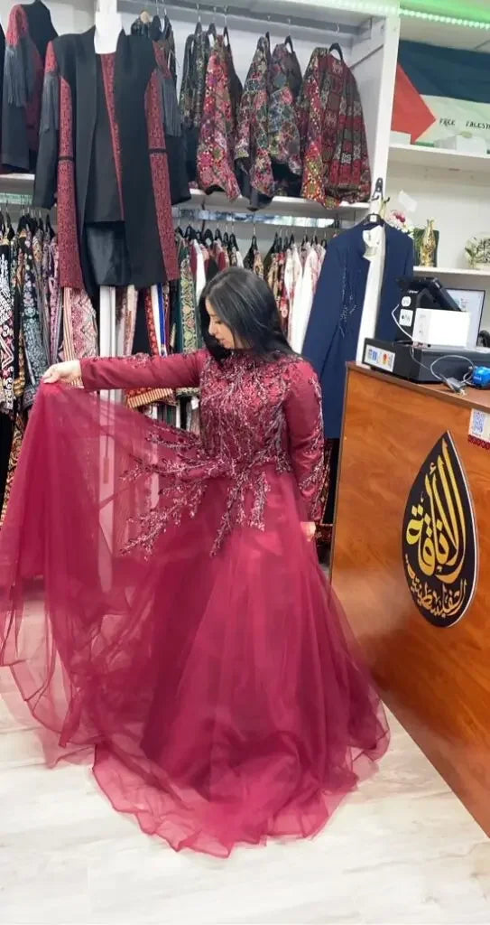 Woman wearing a burgundy Palestinian embroidered dress with intricate detailing and tulle skirt in a boutique