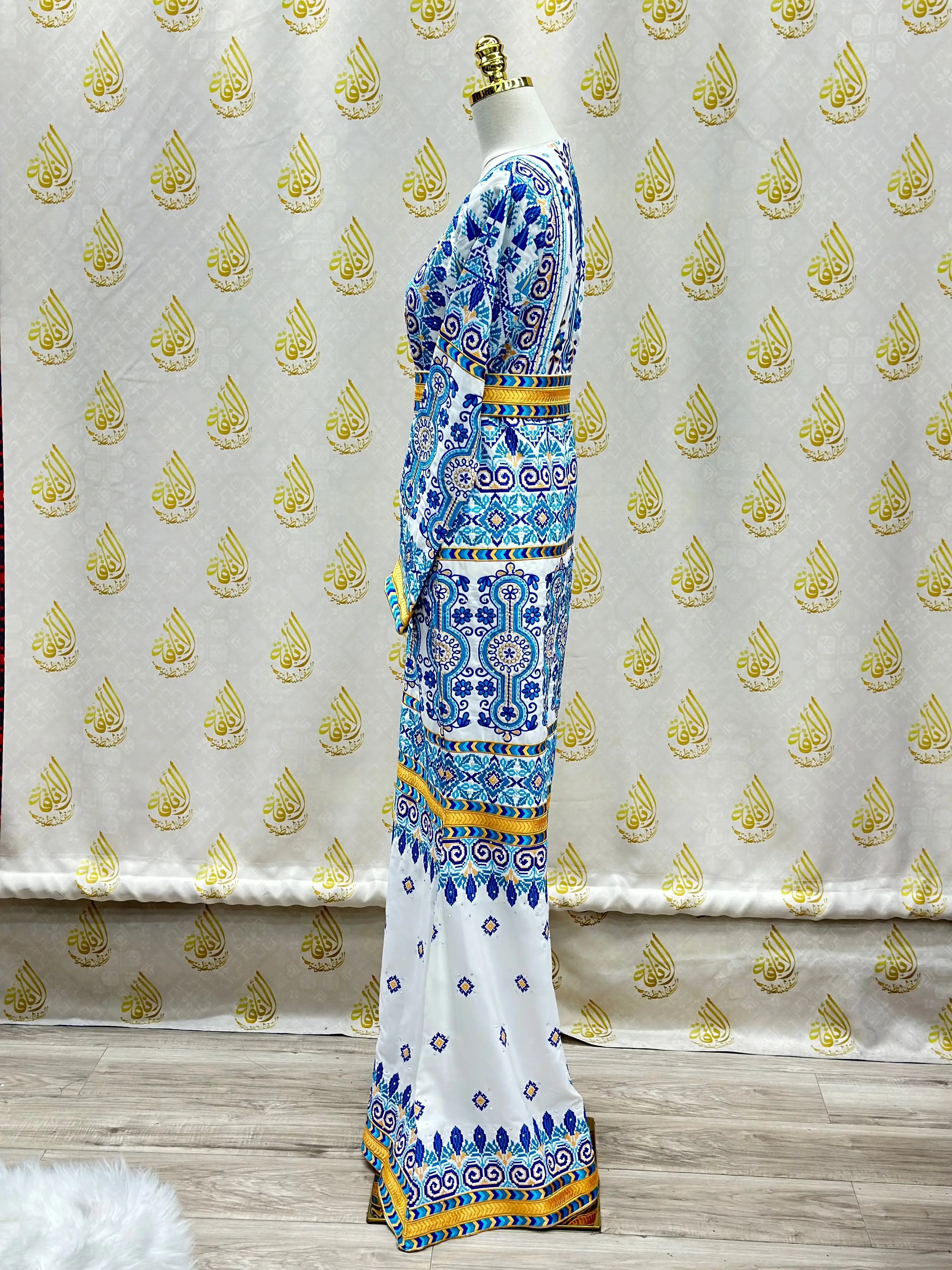 Palestinian embroidered dress by Palestinian Elegance featuring blue and yellow intricate patterns on a long white bridal gown