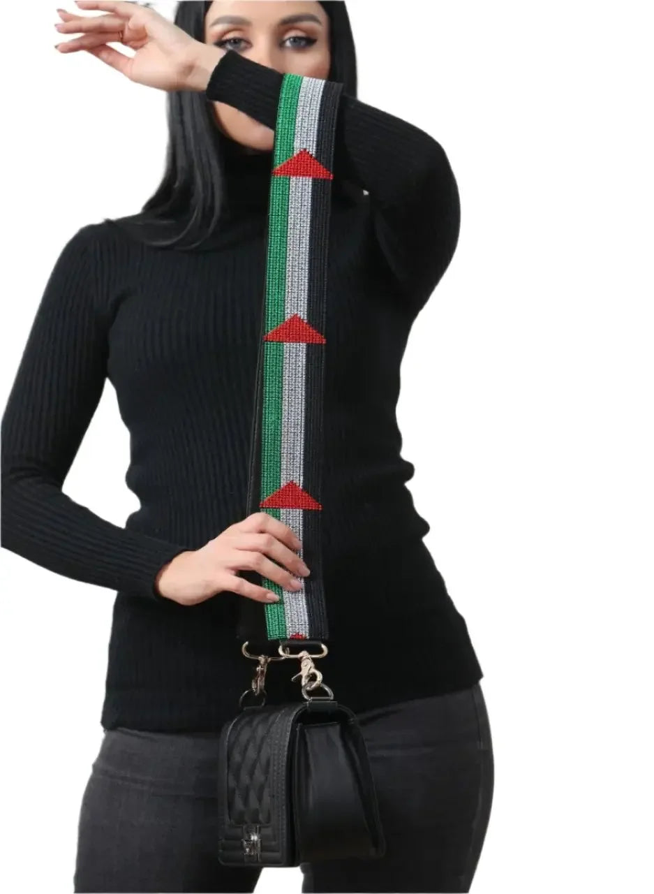 Palestinian embroidered purse strap with green, white, and red patterns held by woman wearing black outfit