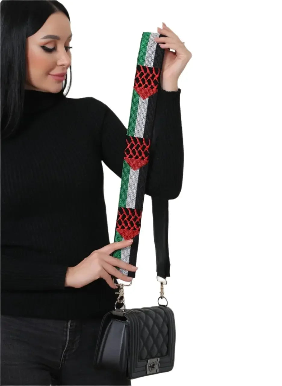 Palestinian embroidered purse strap with traditional red and green patterns held by woman wearing black sweater