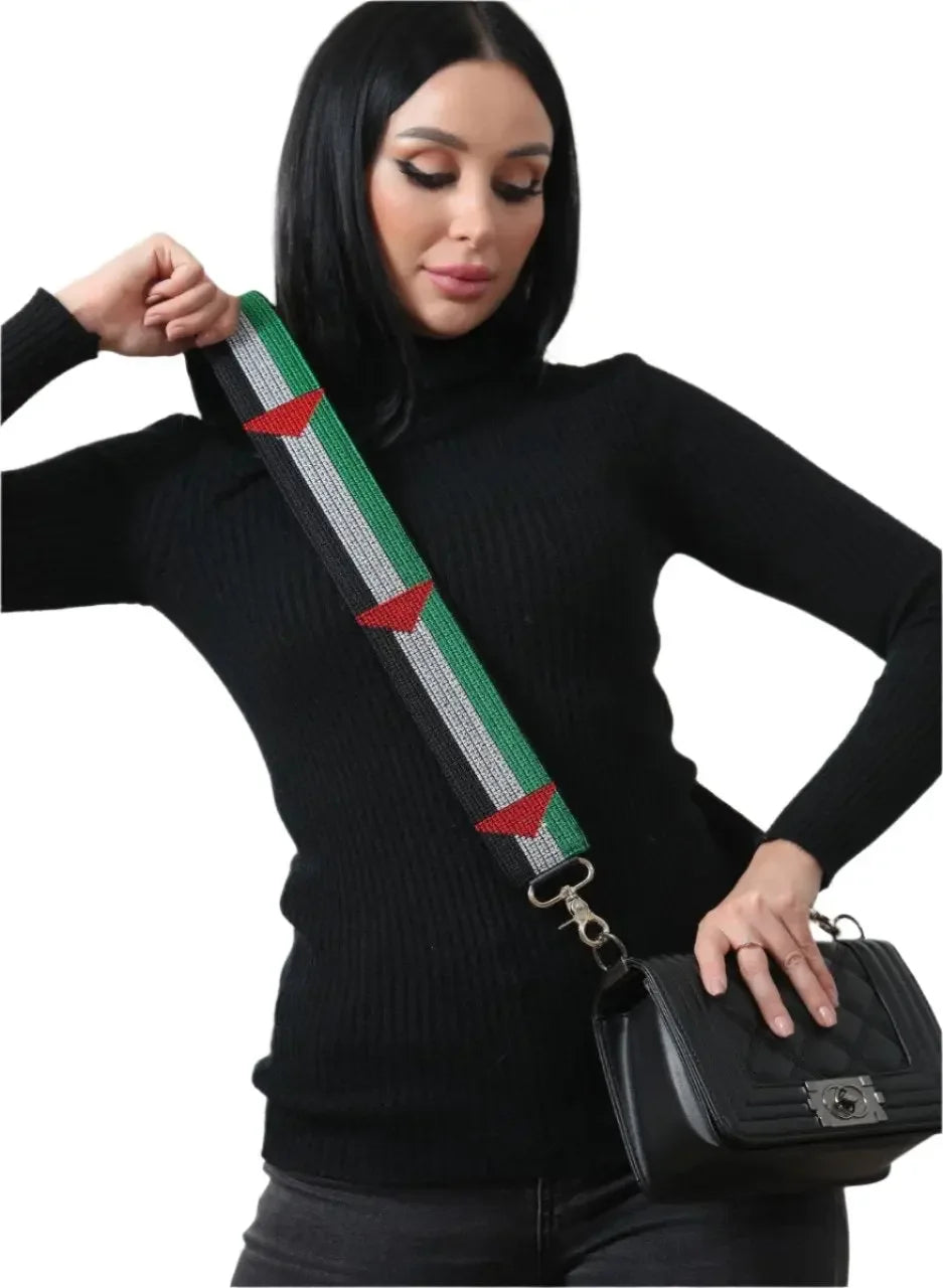 Woman wearing black sweater holding a black purse with a Palestinian embroidered purse strap featuring green, white, and red colors