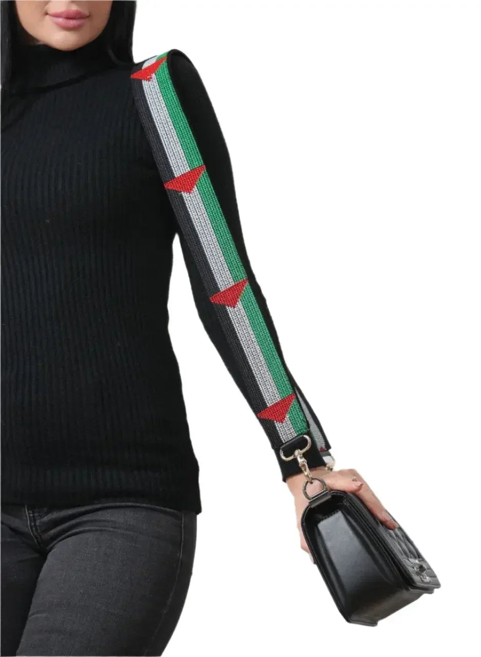 Palestinian embroidered purse strap in red green white colors attached to black purse held by woman in black outfit