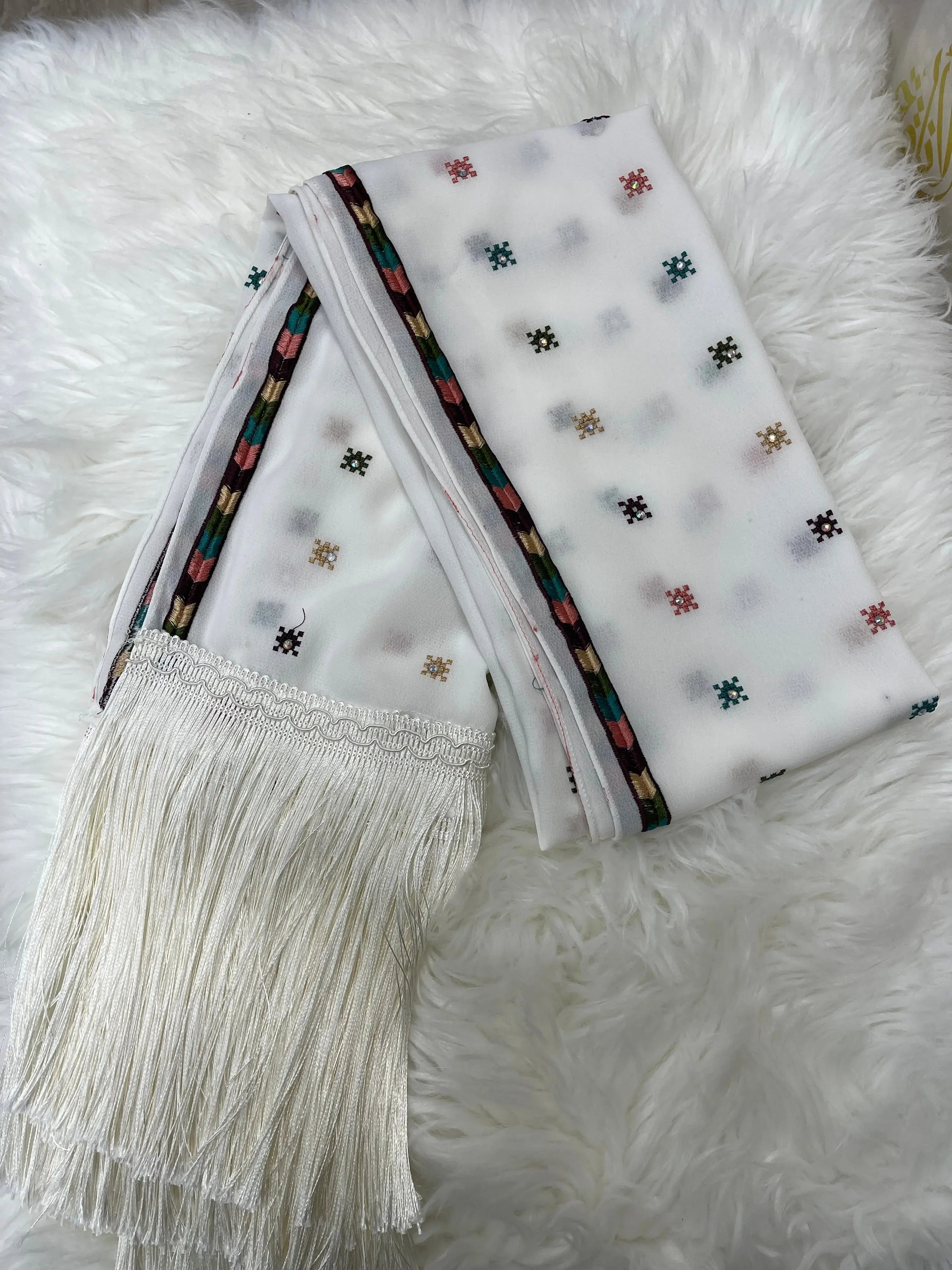 Palestinian embroidered shawl with multicolor embroidery and white fringe laid on white fur background