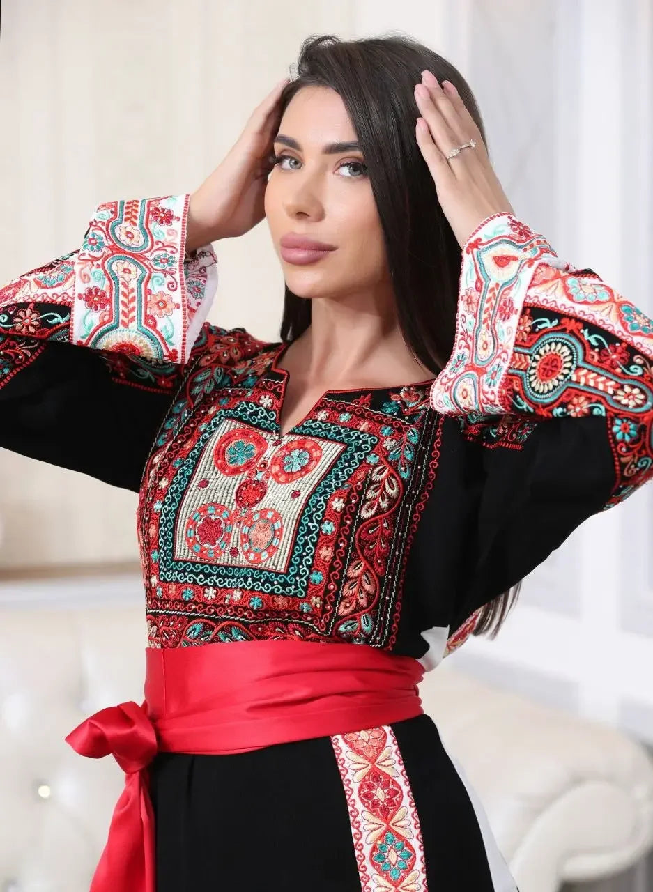 Woman wearing a Palestinian embroidered thobe with intricate red and green embroidery and a red sash
